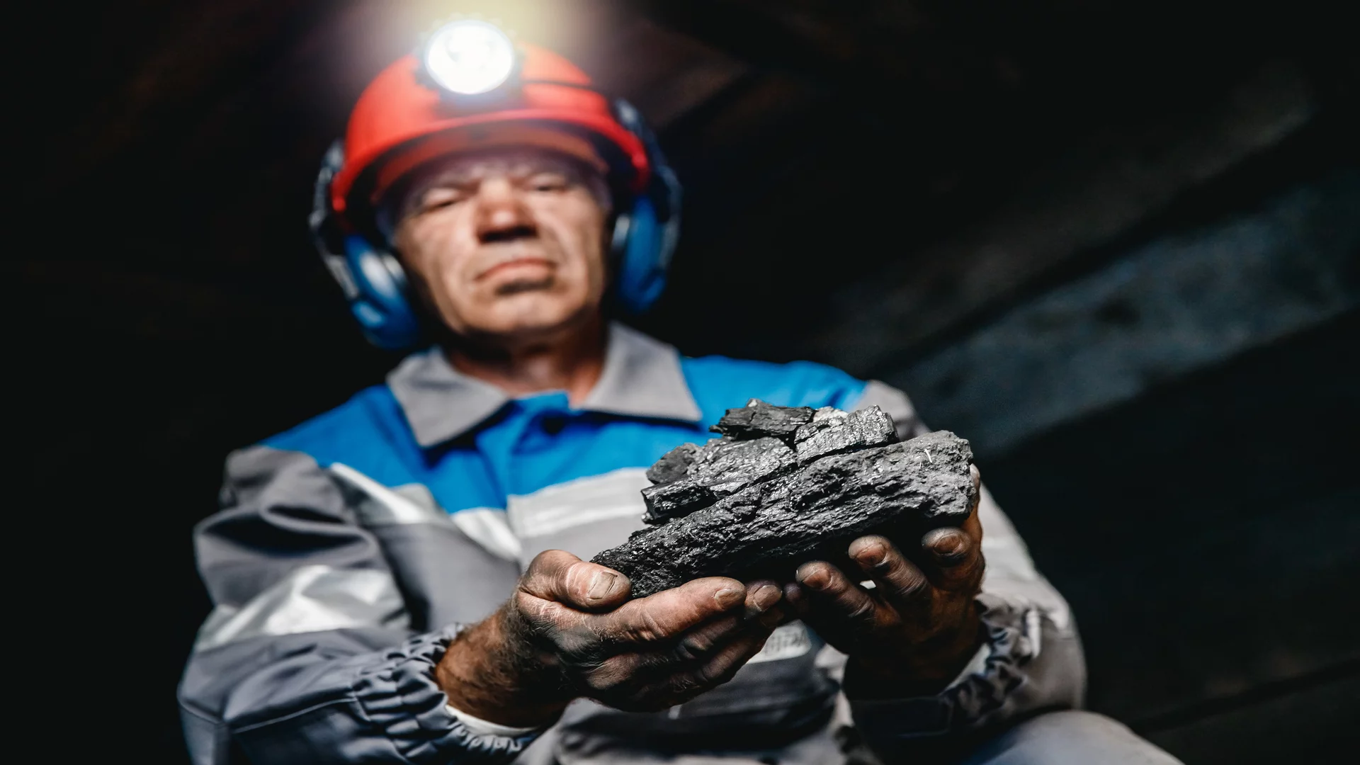 Górnik trzymający bryłę węgla w kopalni. W niebieskim kombinezonie.