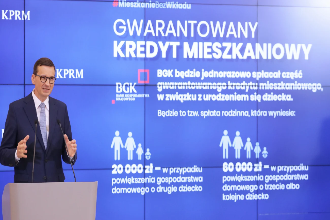 Mateusz Morawiecki przemawia na konferencji prasowej Polskiego ładu na tle niebieskiego telebimu