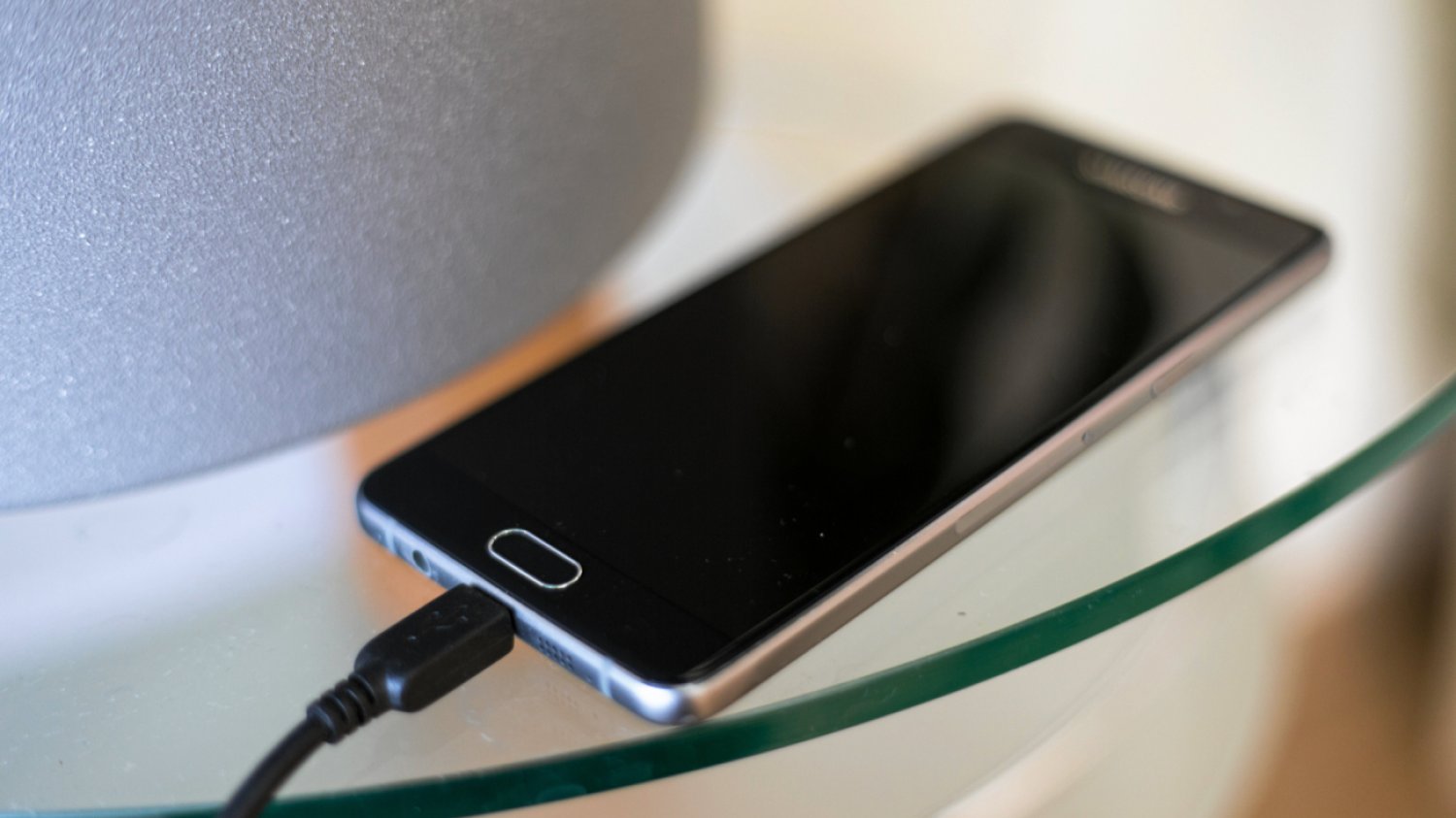 Smartfon ładujący się na szklanym stoliku.