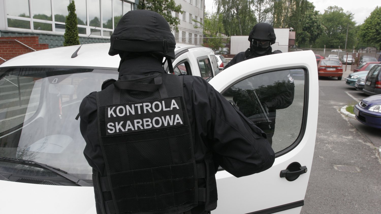 Agenci kontroli skarbowej w czarnych kombinezonach wsiadają do białego auta