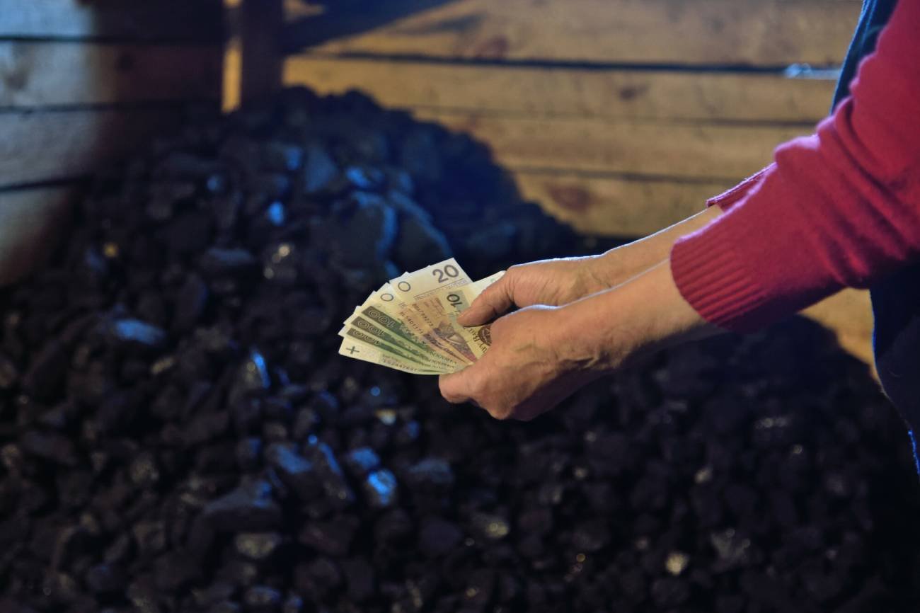 Emerytka pokazuje pieniądze na tle węgla w piwnicy
