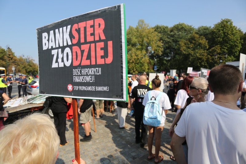 Demonstracja frankowiczów przeciwko bankom. Na pierwszym planie baner z biało-czerwonym napisem "bankster złodziej"