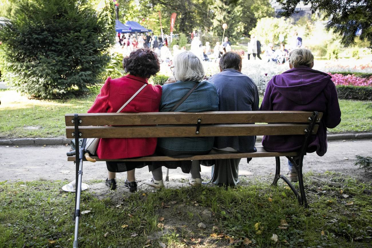 Cztery seniorki siedzą na ławce w parku i rozmawiają.