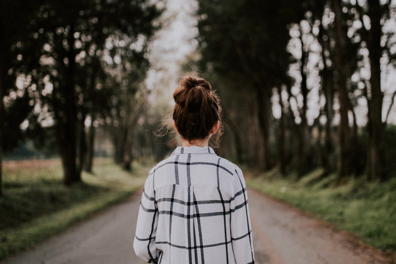 Kobieta odwrócona plecami stojąca na początku prostej drogi