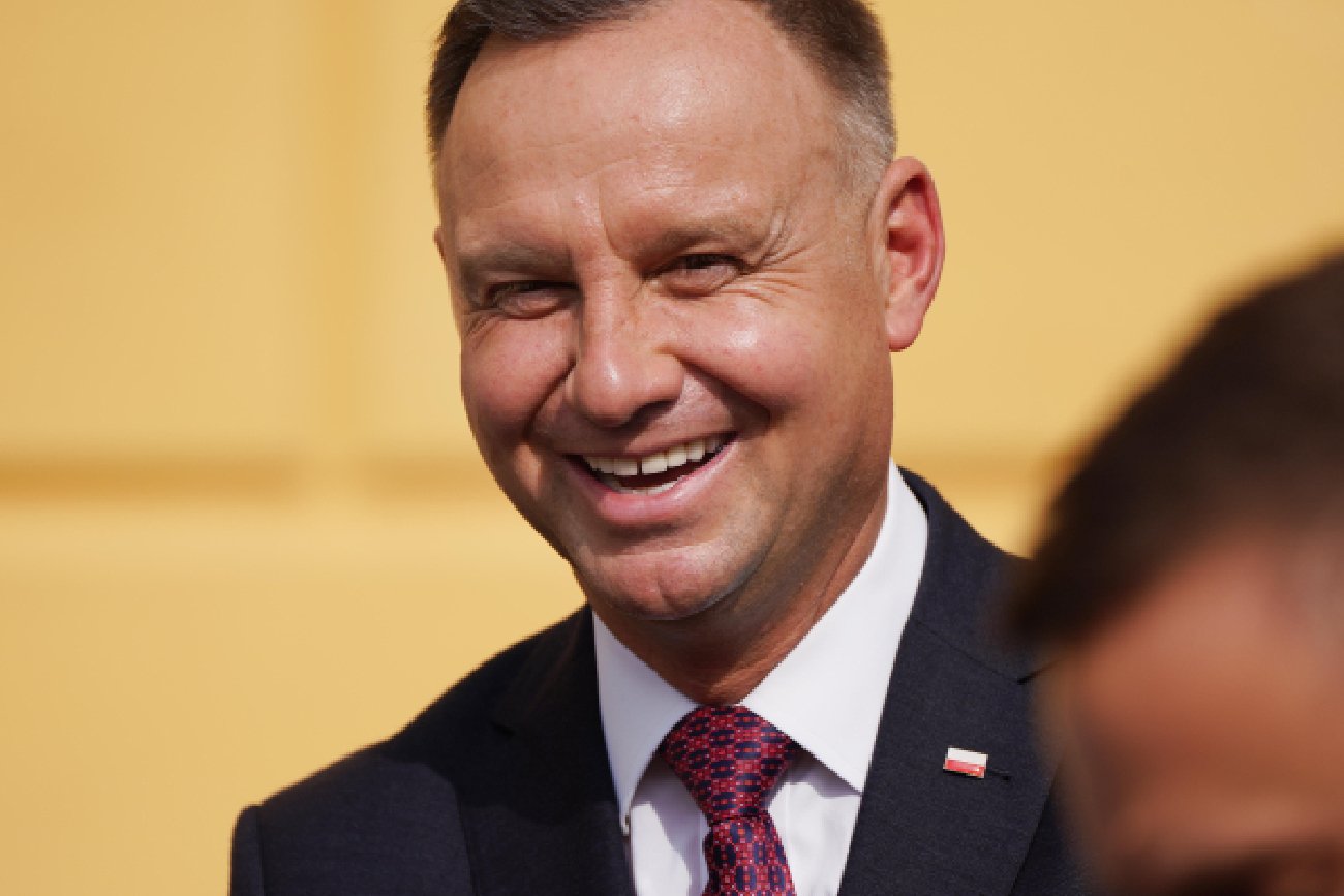 uśmiechnięty prezydent Polski Andrzej Duda na tle pomarańczowej ściany