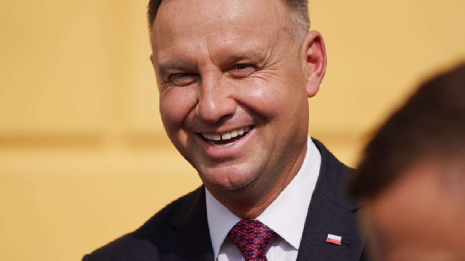 uśmiechnięty prezydent Polski Andrzej Duda na tle pomarańczowej ściany