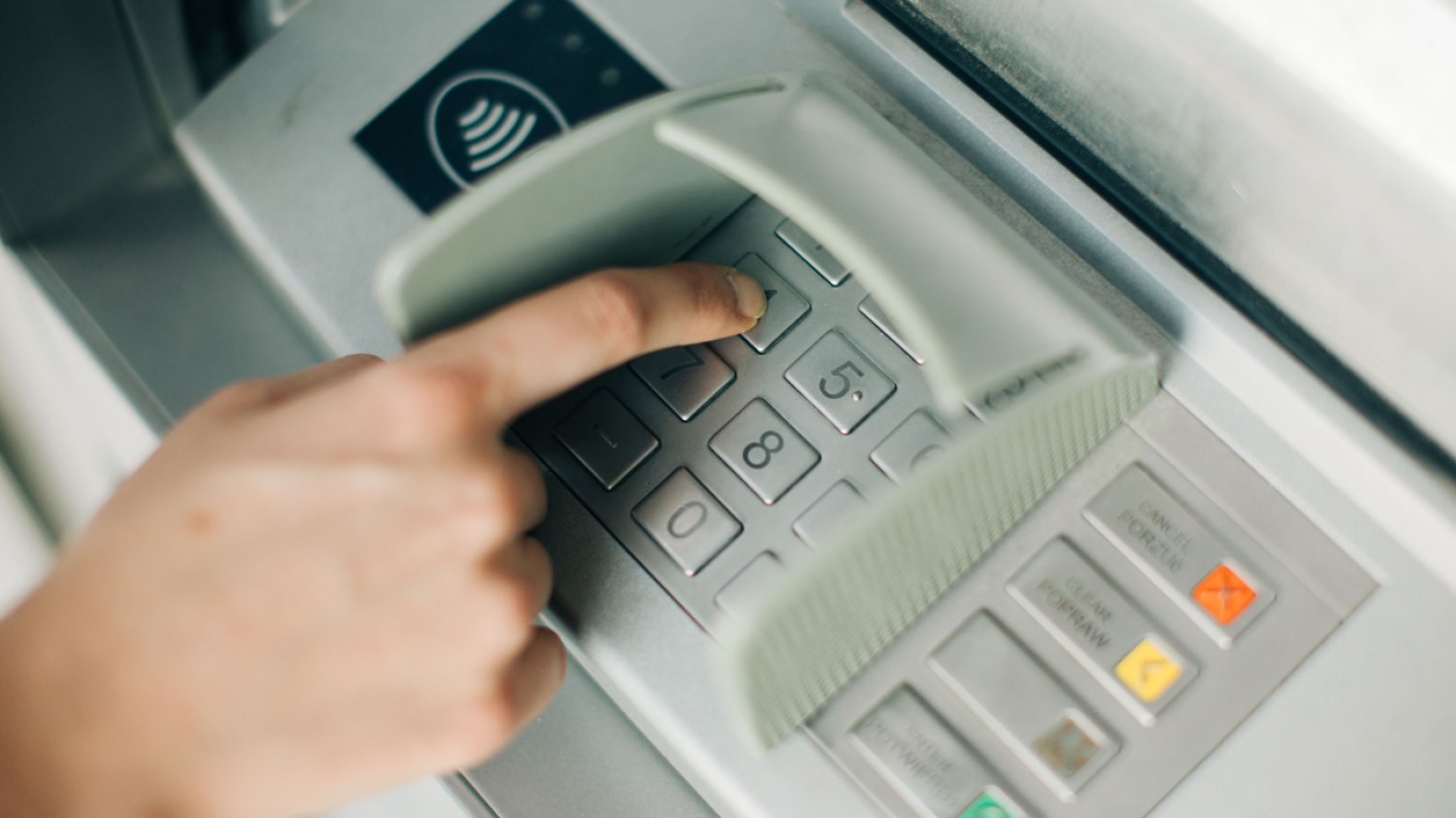 Ręka osoby wpisującej PIN w bankomacie