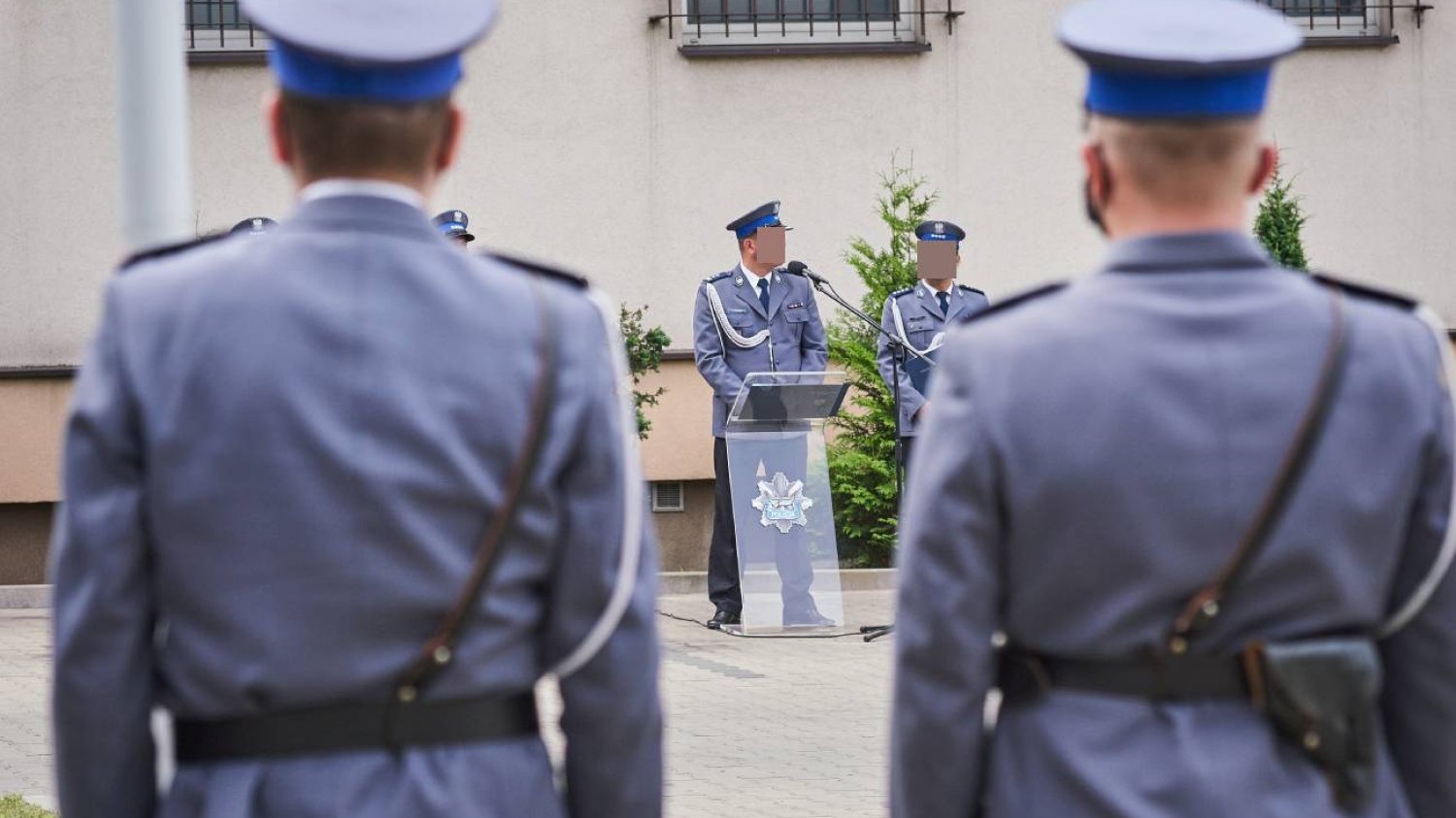 Policjanci w mundurach stoją przed budynkiem.