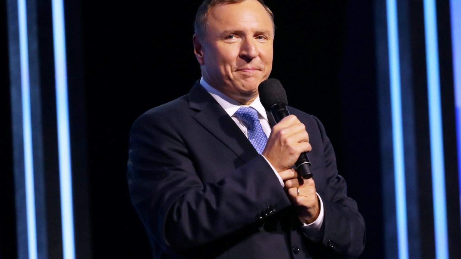 Jacek Kurski prezes Telewizji Polskiej stoi na tle wysokiego budynku i trzyma w dłoniach maseczkę