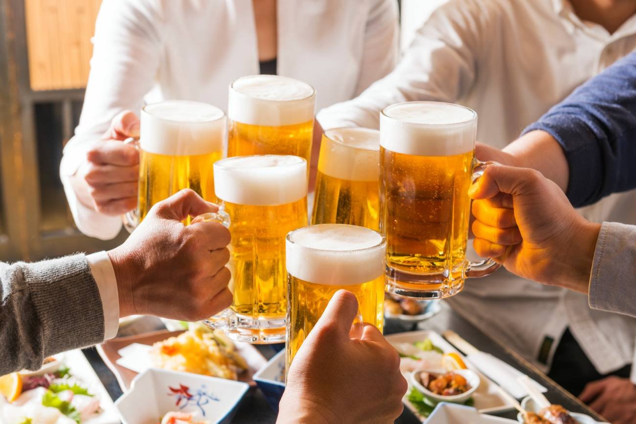 Ludzie przy stole wznoszą toast kuflami z piwem