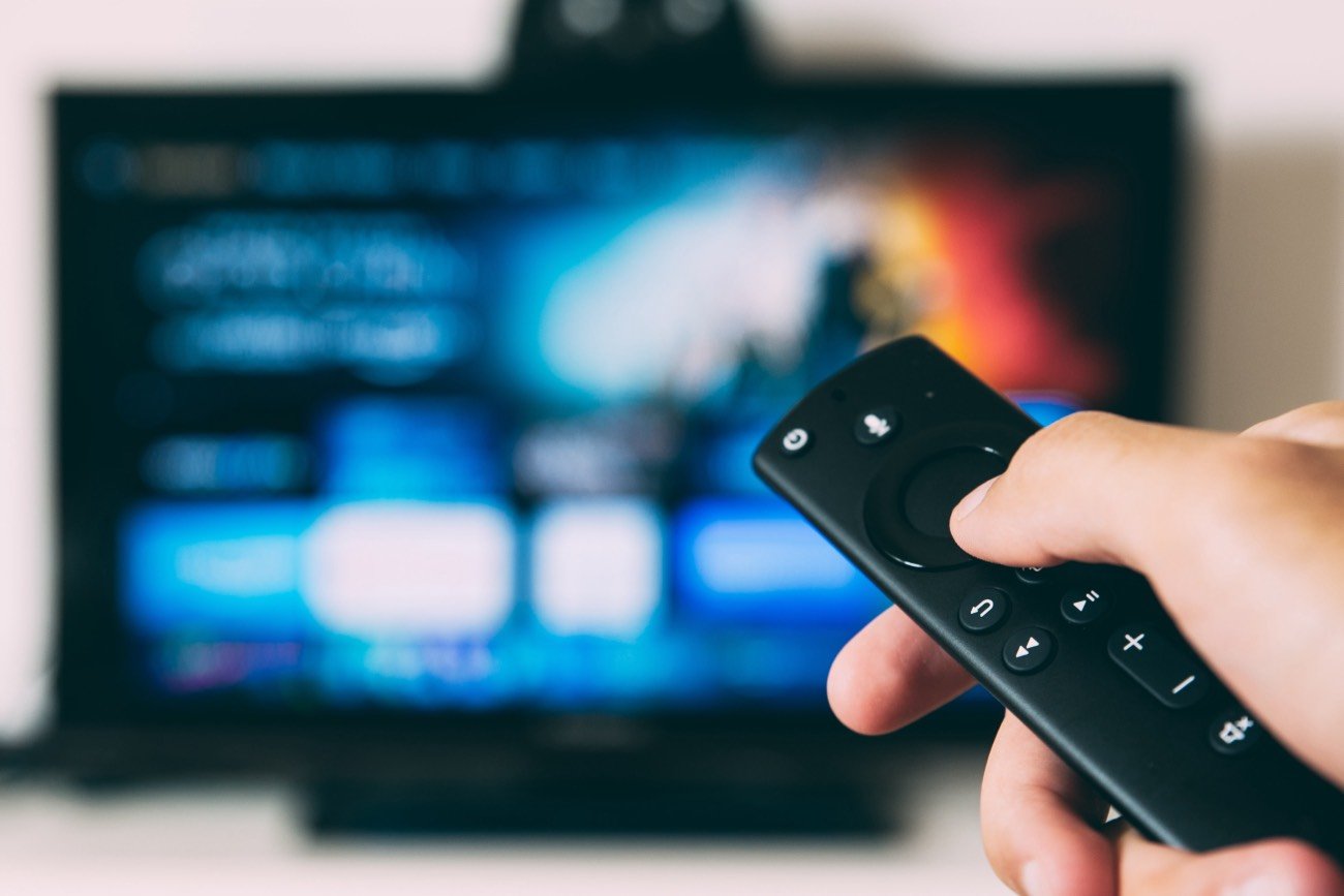 Ręka z pilotem do telewizora, w tle telewizor