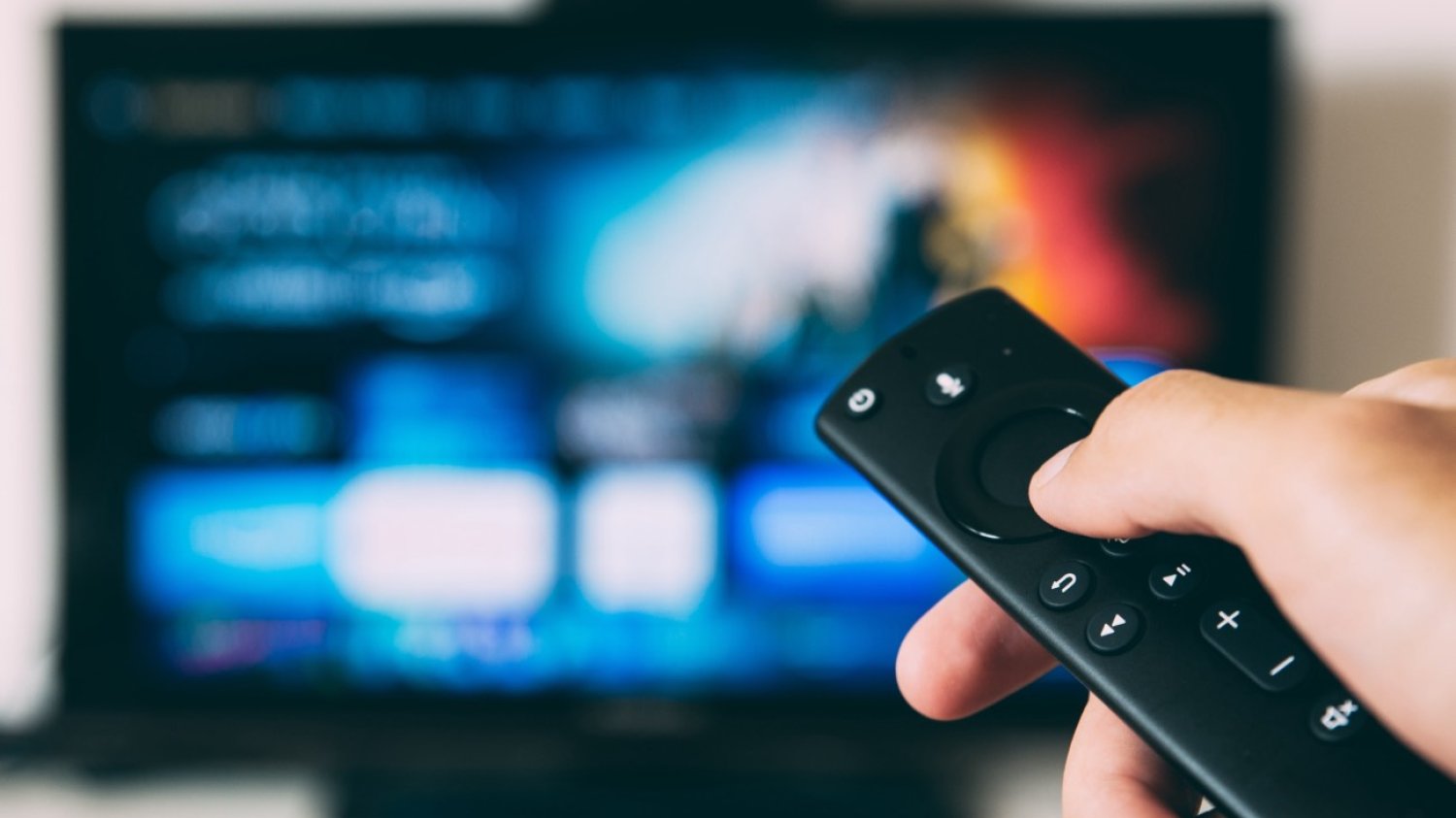 Ręka z pilotem do telewizora, w tle telewizor