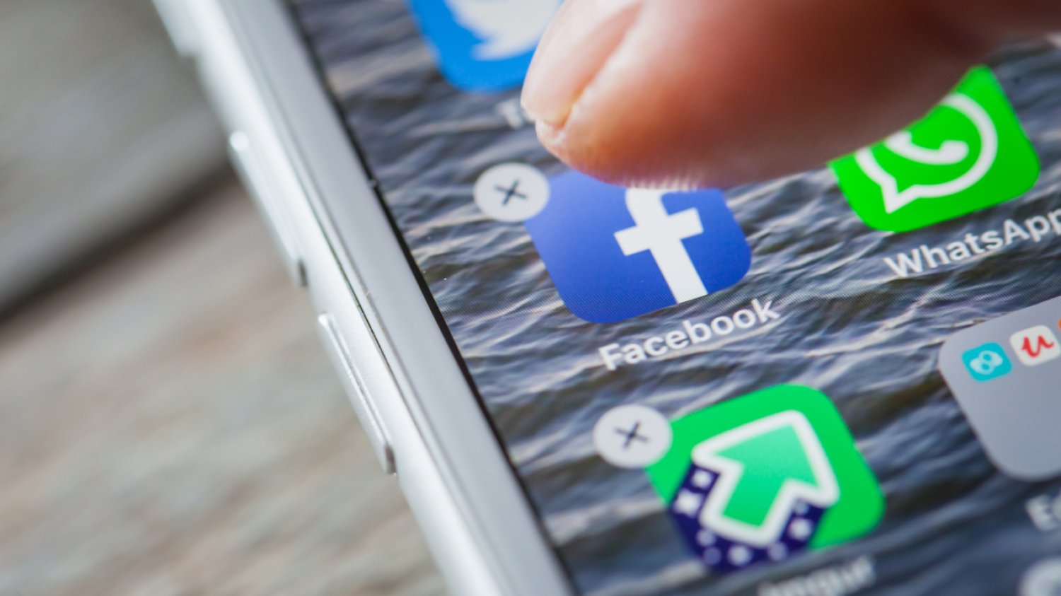 palec człowieka chce kliknąć w ikonę Facebooka, która wyświetla się na ekranie samrtphona