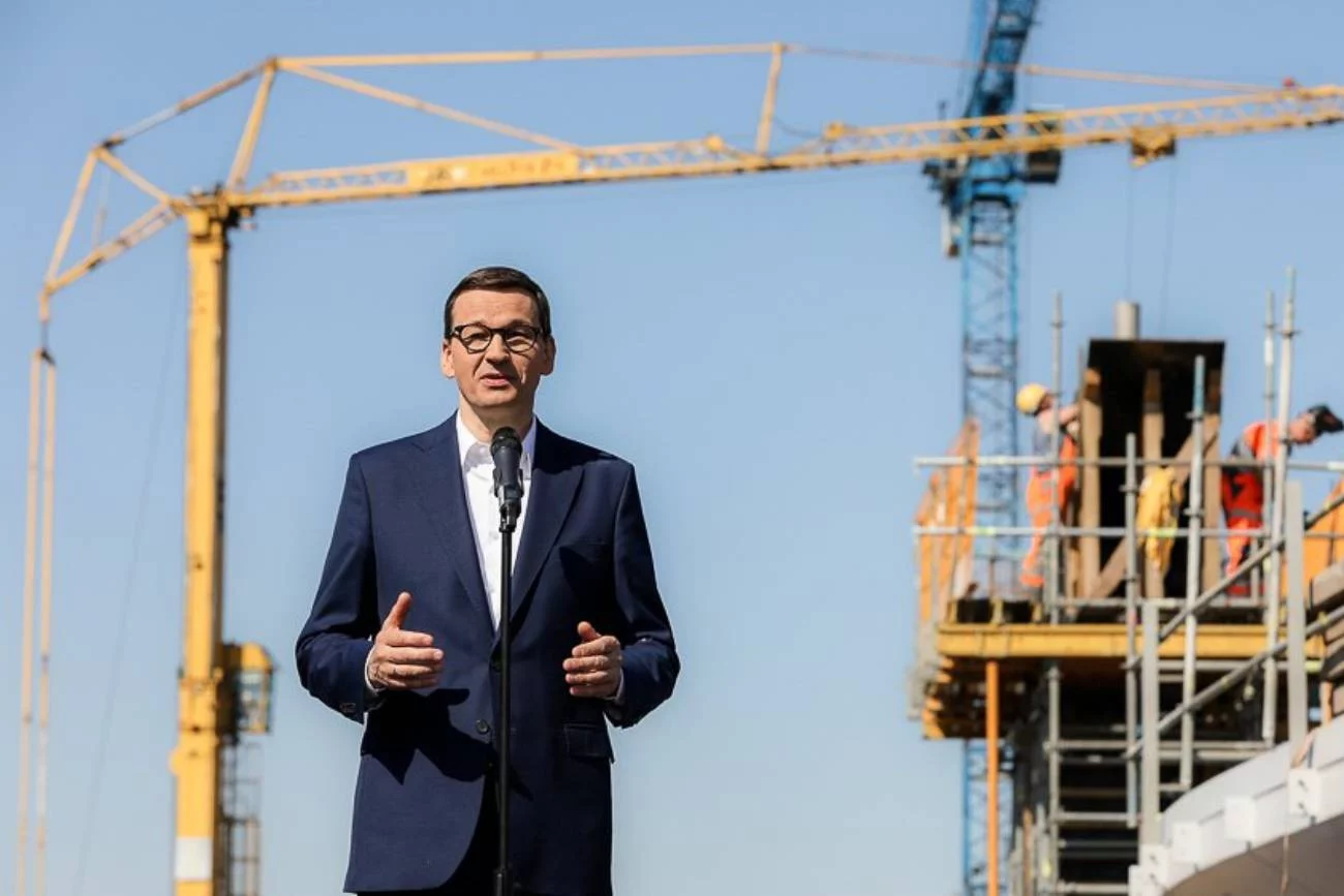 Premier Mateusz Morawiecki przemawia na tle budowy. W tle dźwig, robotnicy.