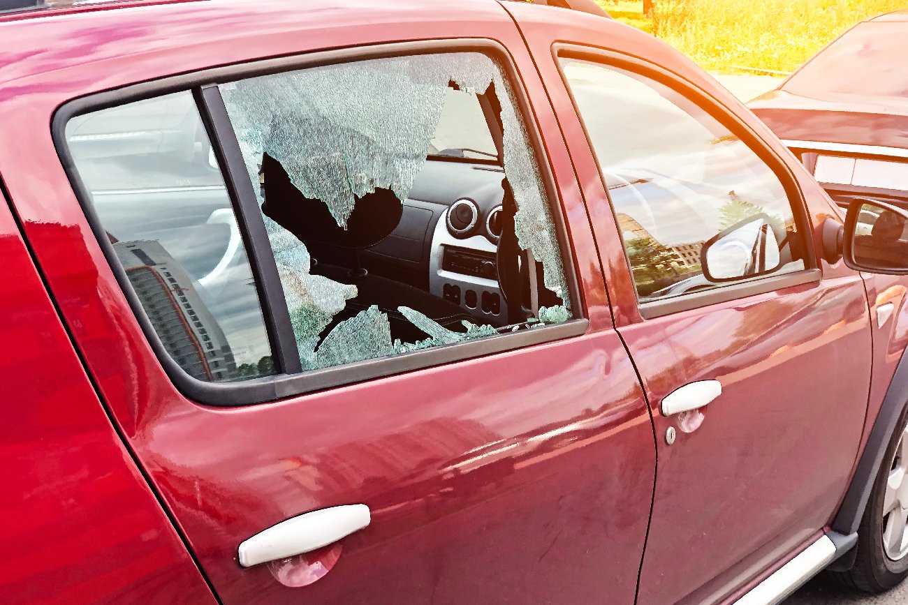 rozbite szkło na drzwiach pasażera zaparkowanego czerwonego samochodu osobowego, pojęcie przestępstwa kradzieży samochodu, kradzieży kosztowności, kradzież auta