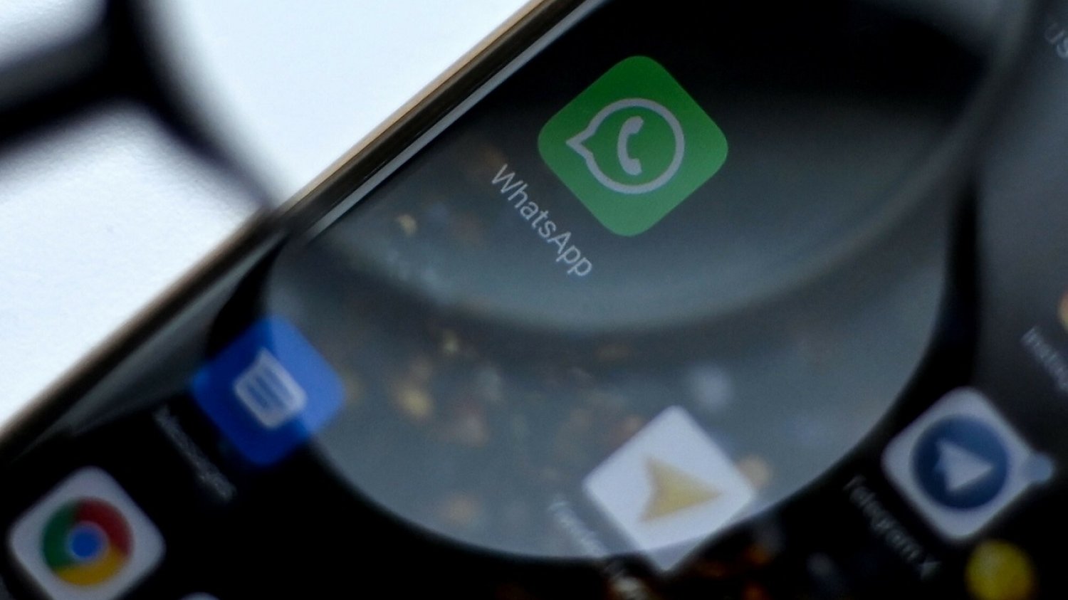 Lupa przybliżona do smartfonu z ikoną WhatsApp.