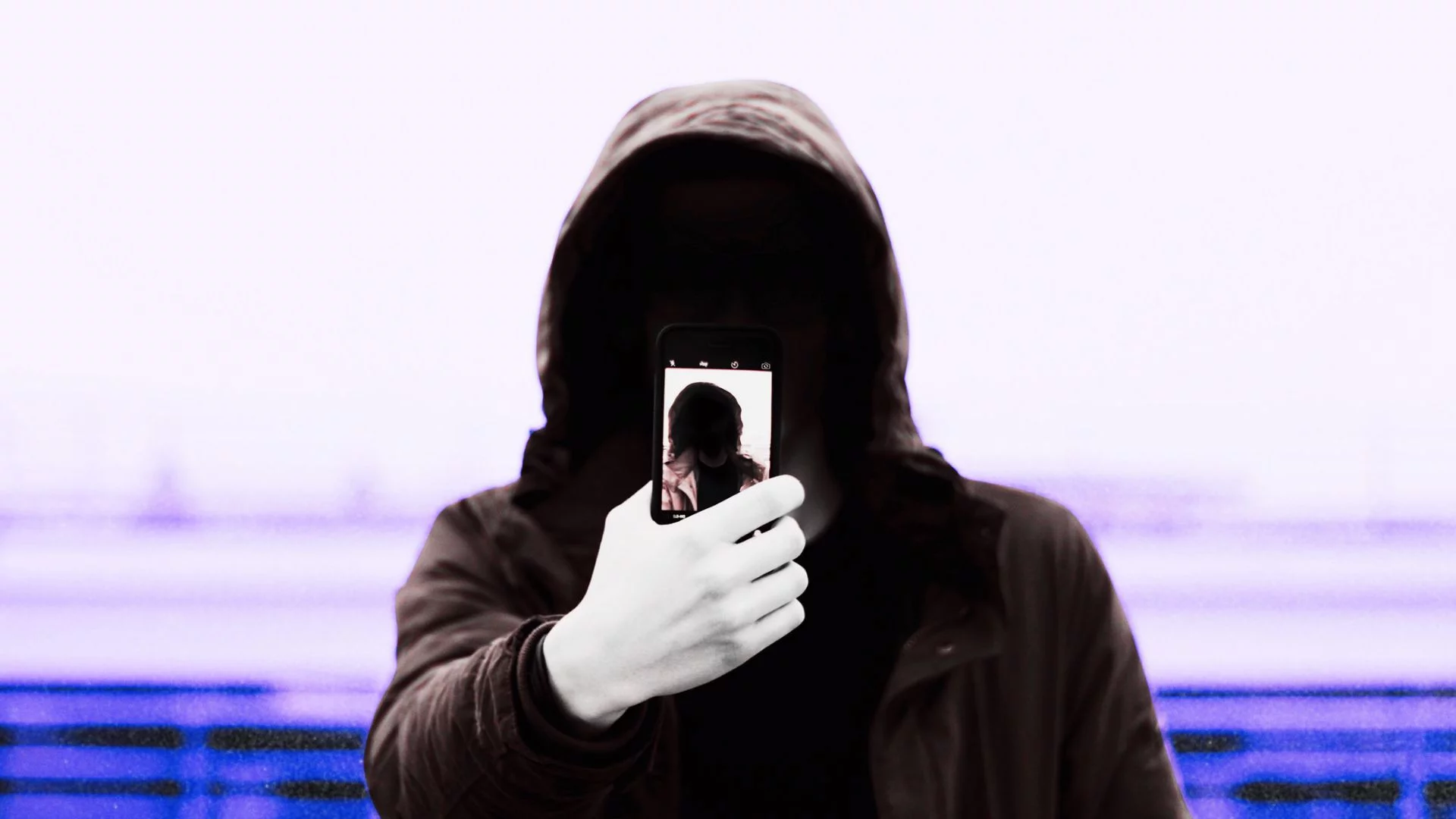 Osoba w kapturze pokazująca ekran smartfona.