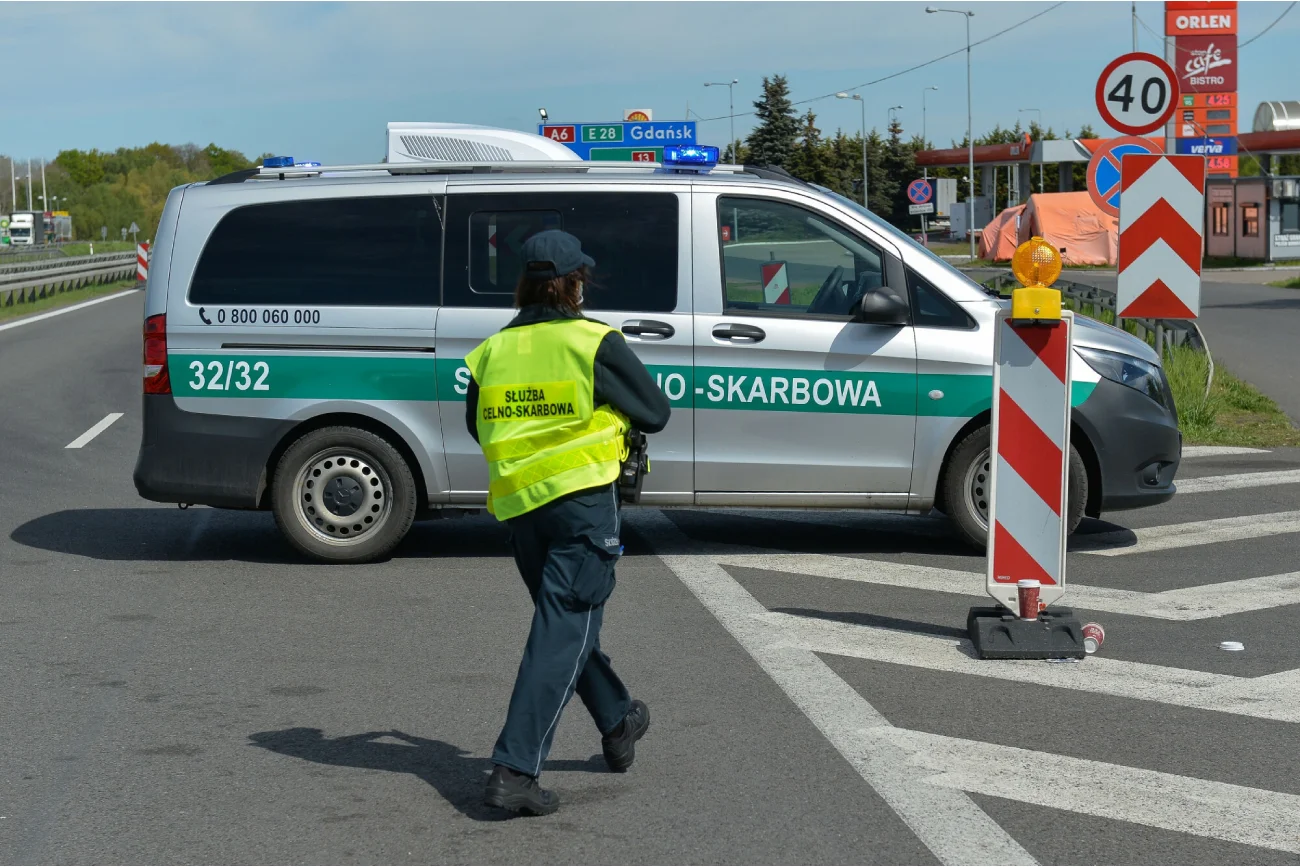 funkcjonariusz izby celno-służbowej w kamizelce odblaskowej idzie w kierunku auta typu bus