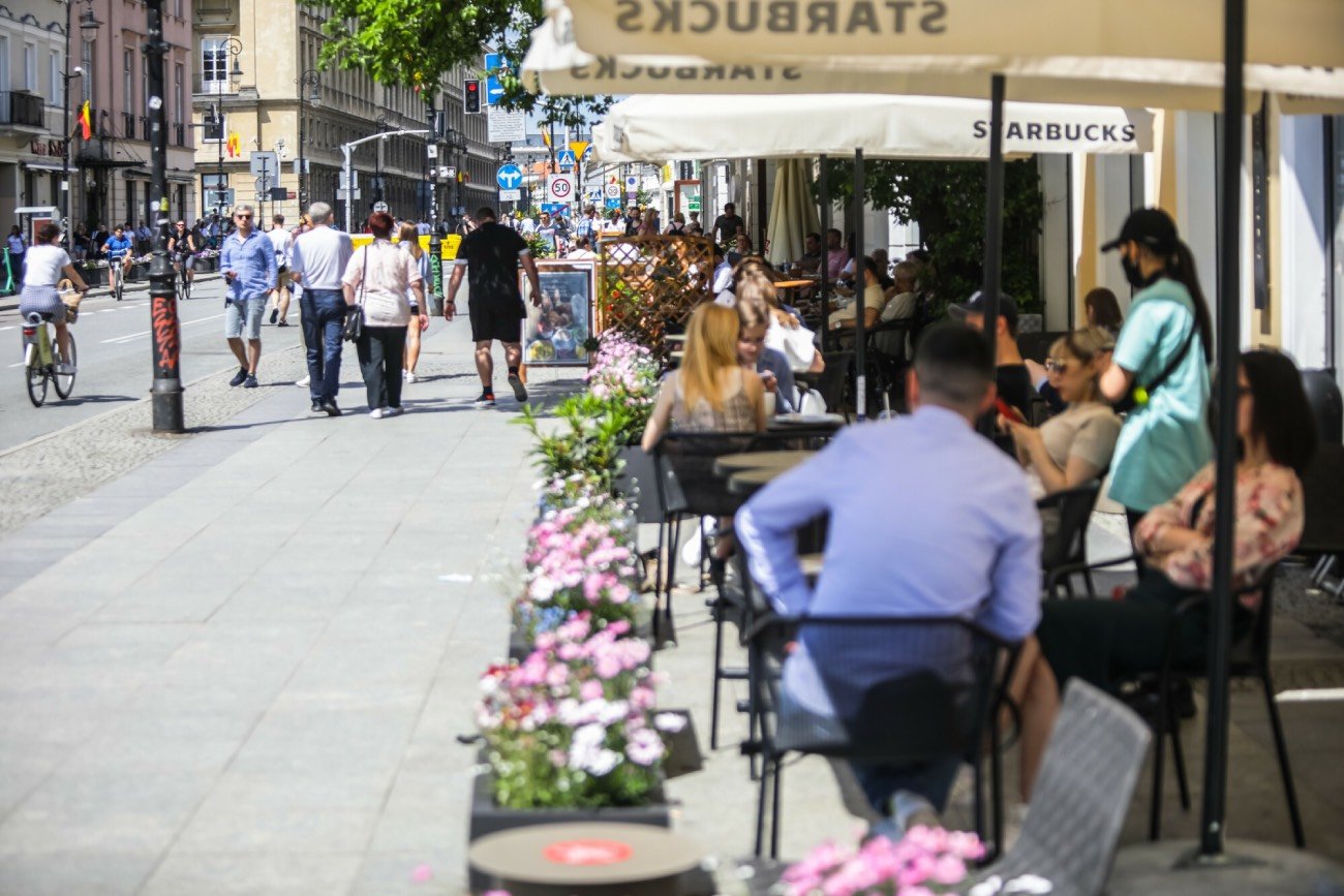 Klienci siedzący w ogródku kawiarnianym w słoneczny dzień