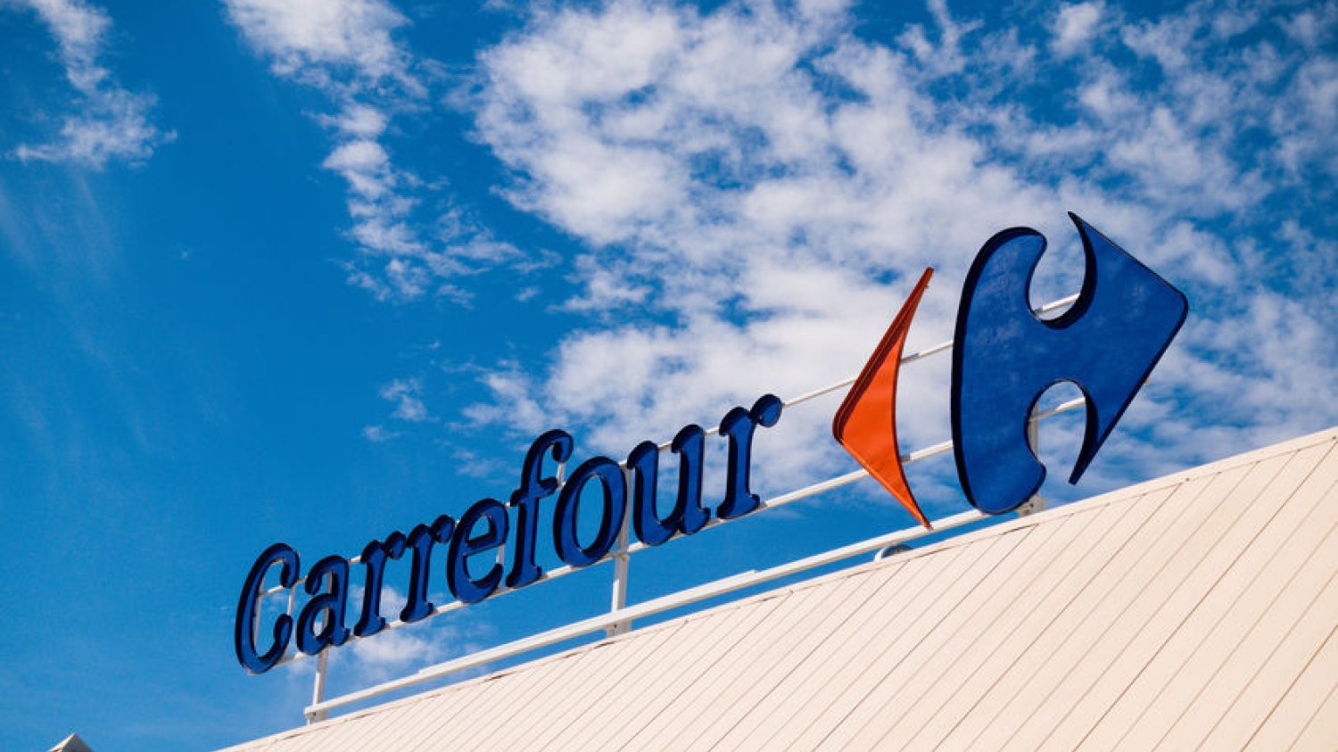 Logo sieci Carrefour na tle błękitnego nieba.