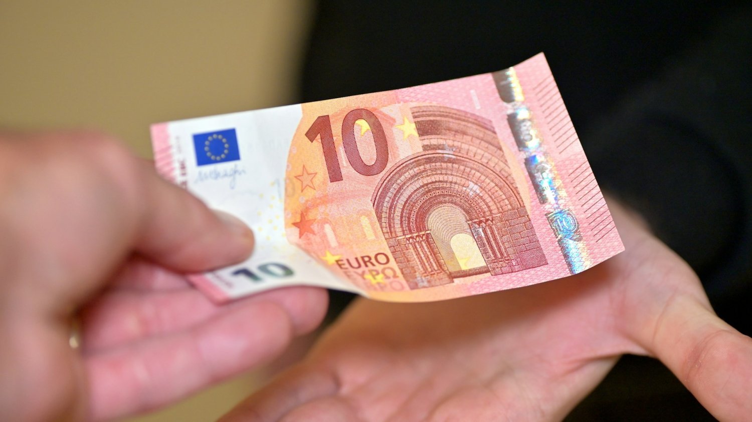 Jedna osoba przekazuje banknot 10 euro do ręki drugiej osobie. W Niemczech chcą ograniczyć świadczenia dla Ukraińców.