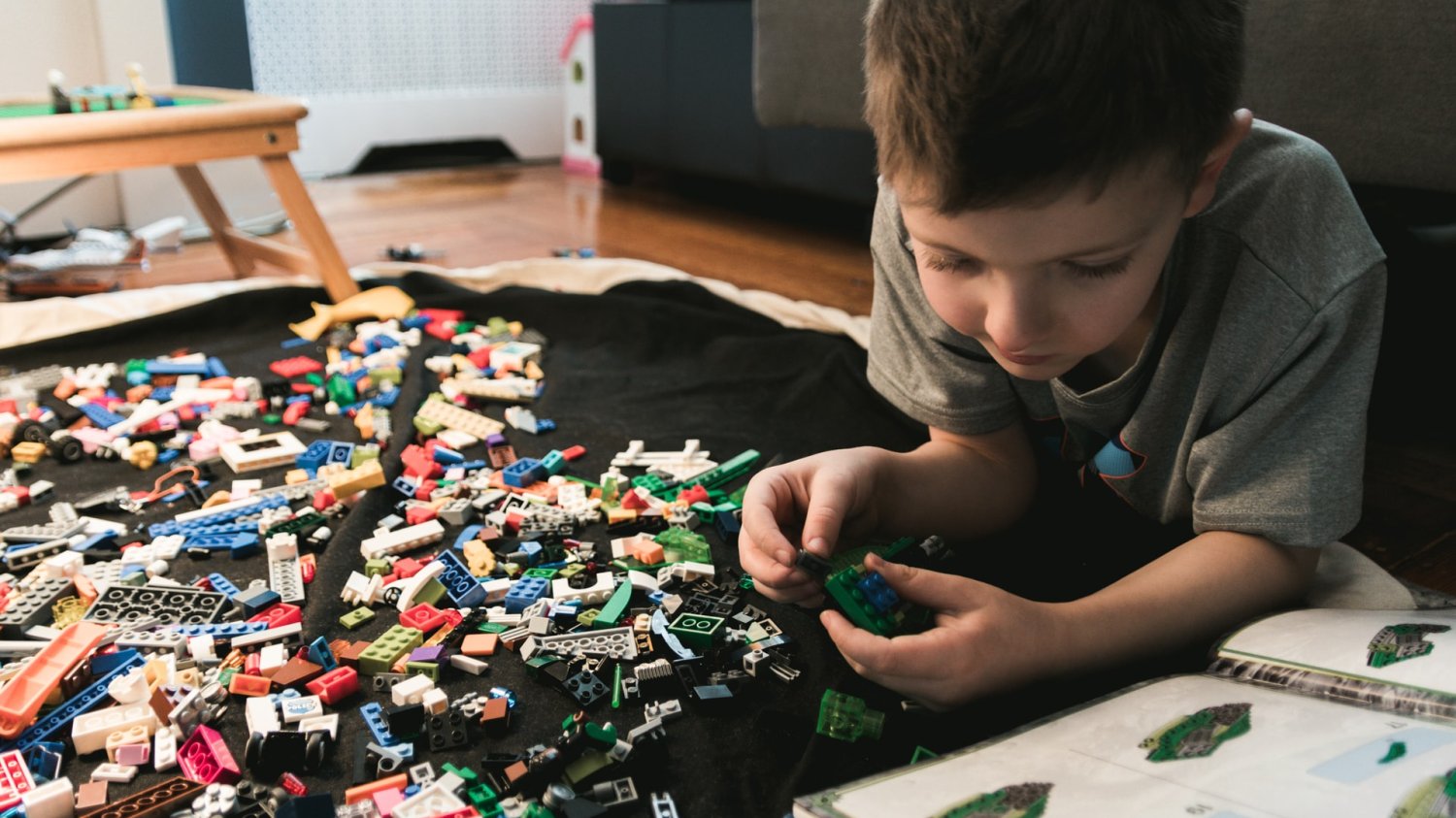 Chłopiec leży na podłodze i układa klocki Lego