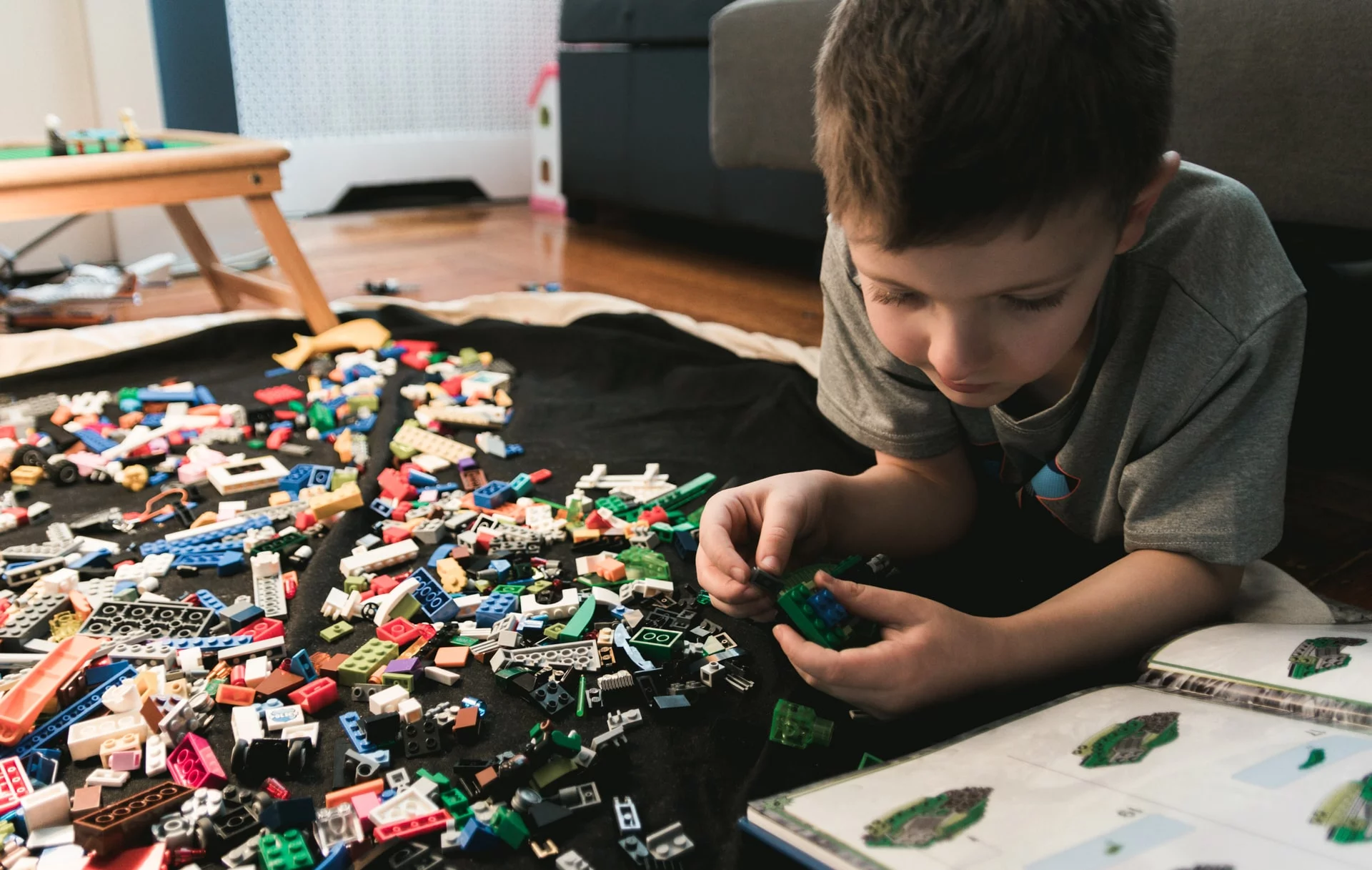 Chłopiec leży na podłodze i układa klocki Lego