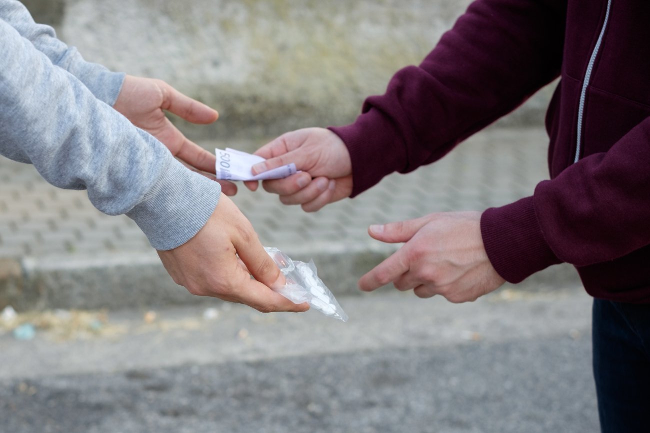 Diler narkotykowy przekazuje klientowi paczuszkę z tabletkami w zamian za pieniądze.