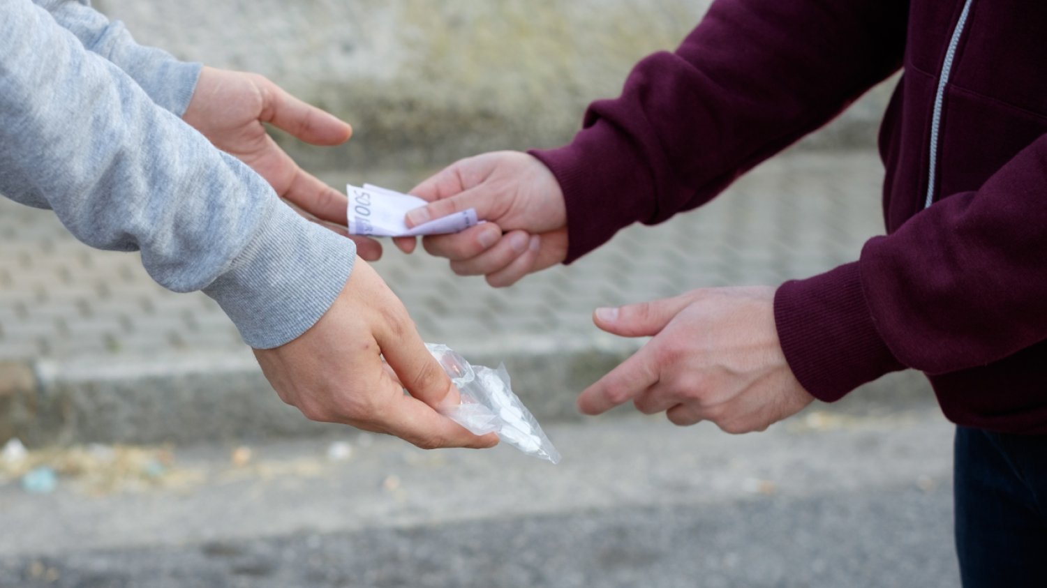 Diler narkotykowy przekazuje klientowi paczuszkę z tabletkami w zamian za pieniądze.
