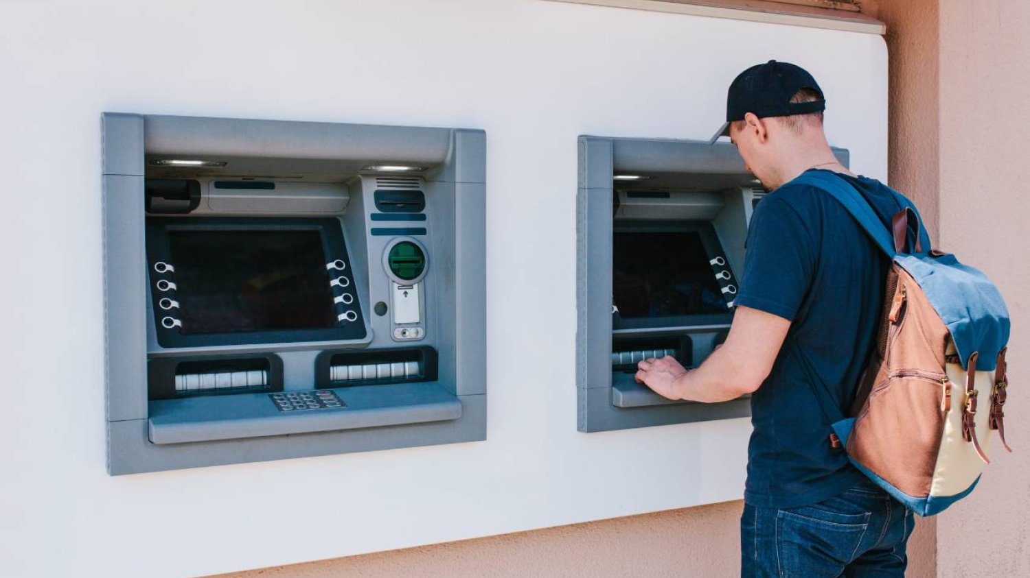 Mężczyzna wyjmuje pieniądze z bankomatu.