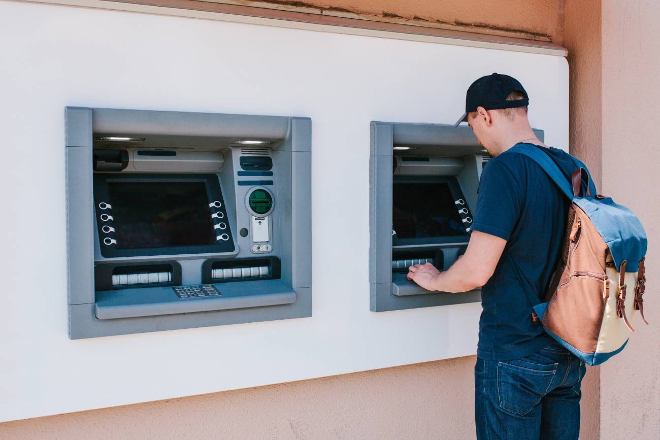 Mężczyzna wyjmuje pieniądze z bankomatu.