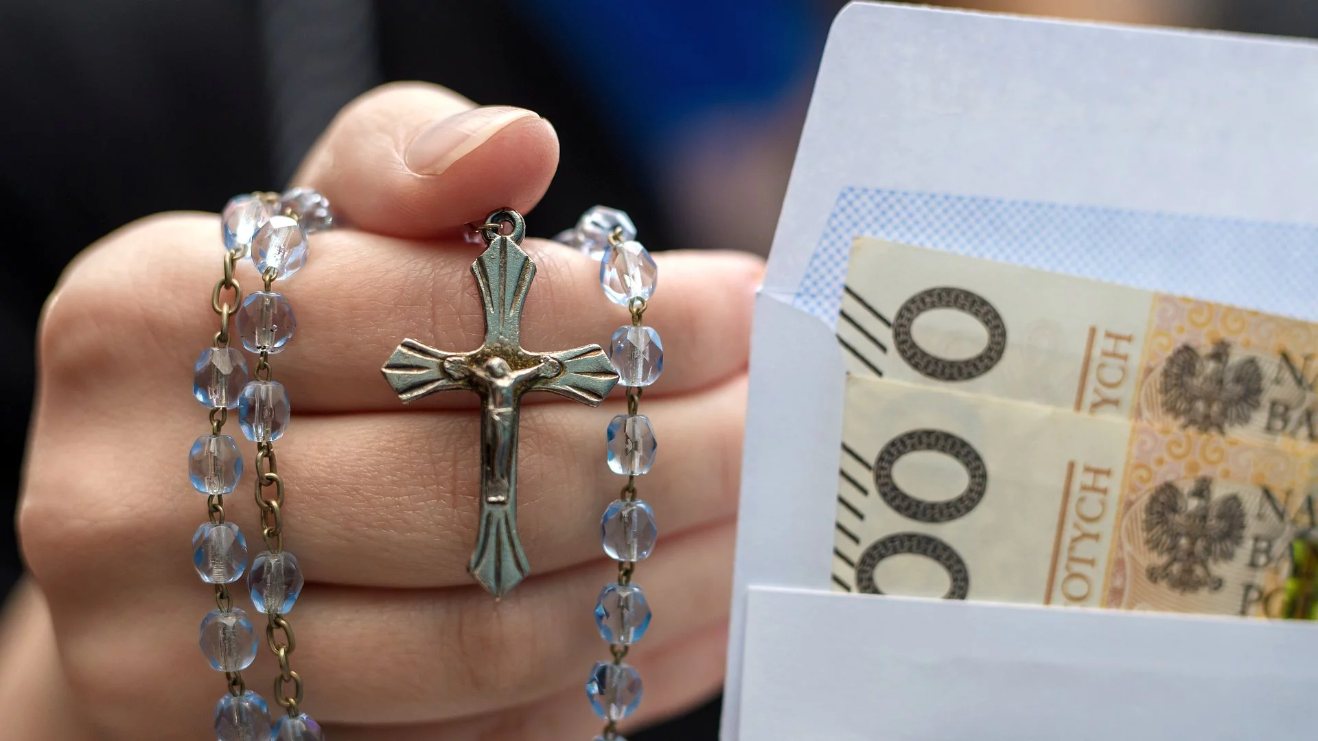 ręka z różańcem i koperta z pieniędzmi