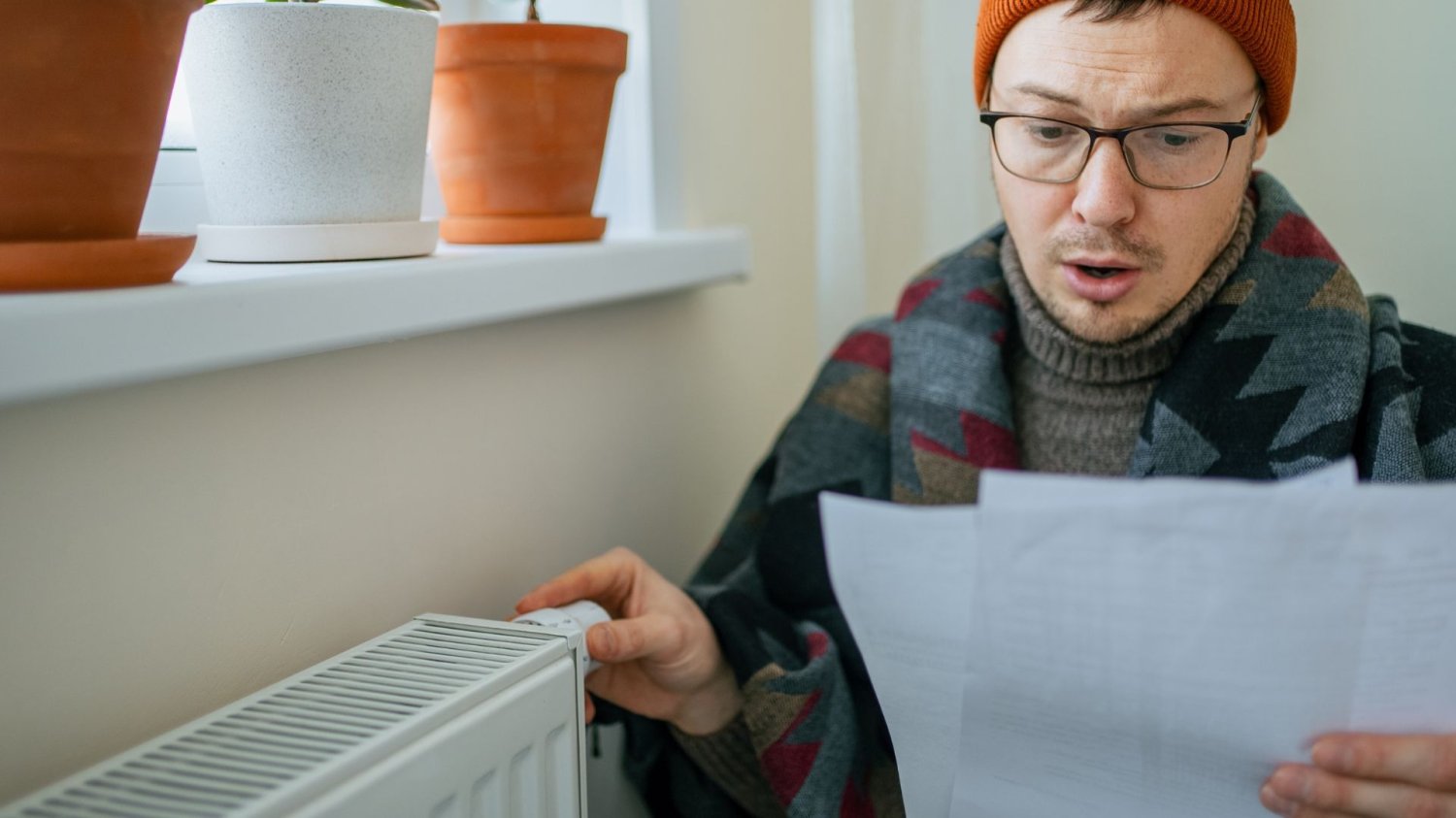 Mężczyzna przykręcający kaloryfer i patrzący na rachunek. Polska może odczuć opłaty za emisje.
