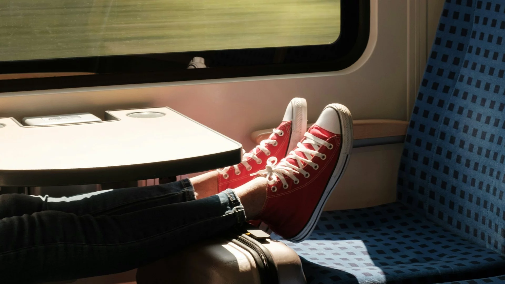 Osoba podróżująca pociągiem z nogami położonymi na walizce przy oknie. Deutsche Bahn ma przejść rewolucję.