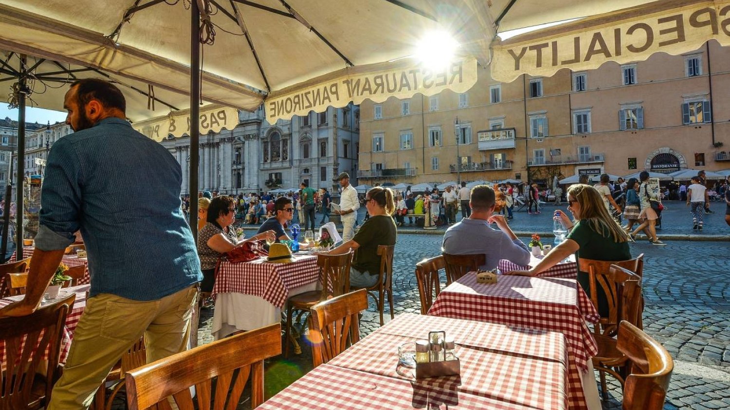 Letni ogródek restauracyjny. Kelner obsługujący gości.