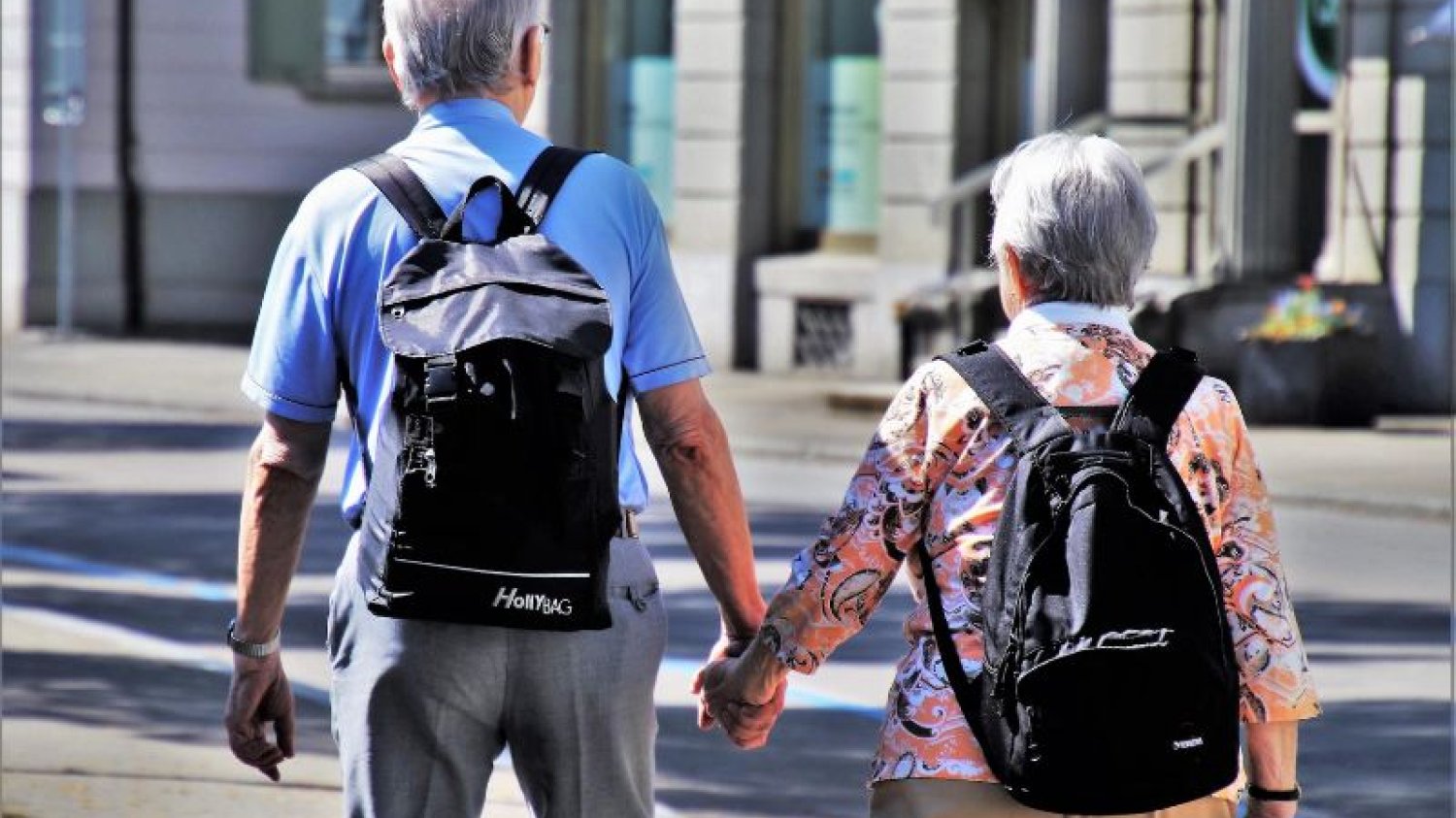 Para seniorów trzymająca się za ręce z plecakami na plecach.
