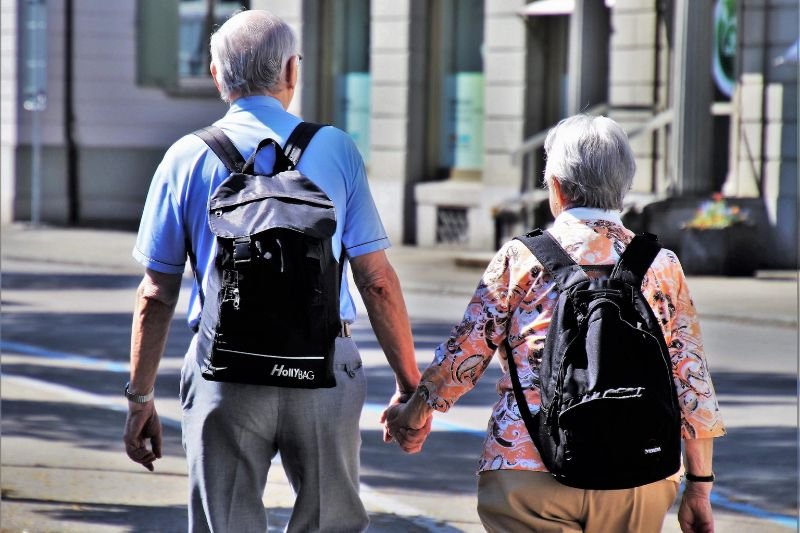 Para seniorów trzymająca się za ręce z plecakami na plecach.