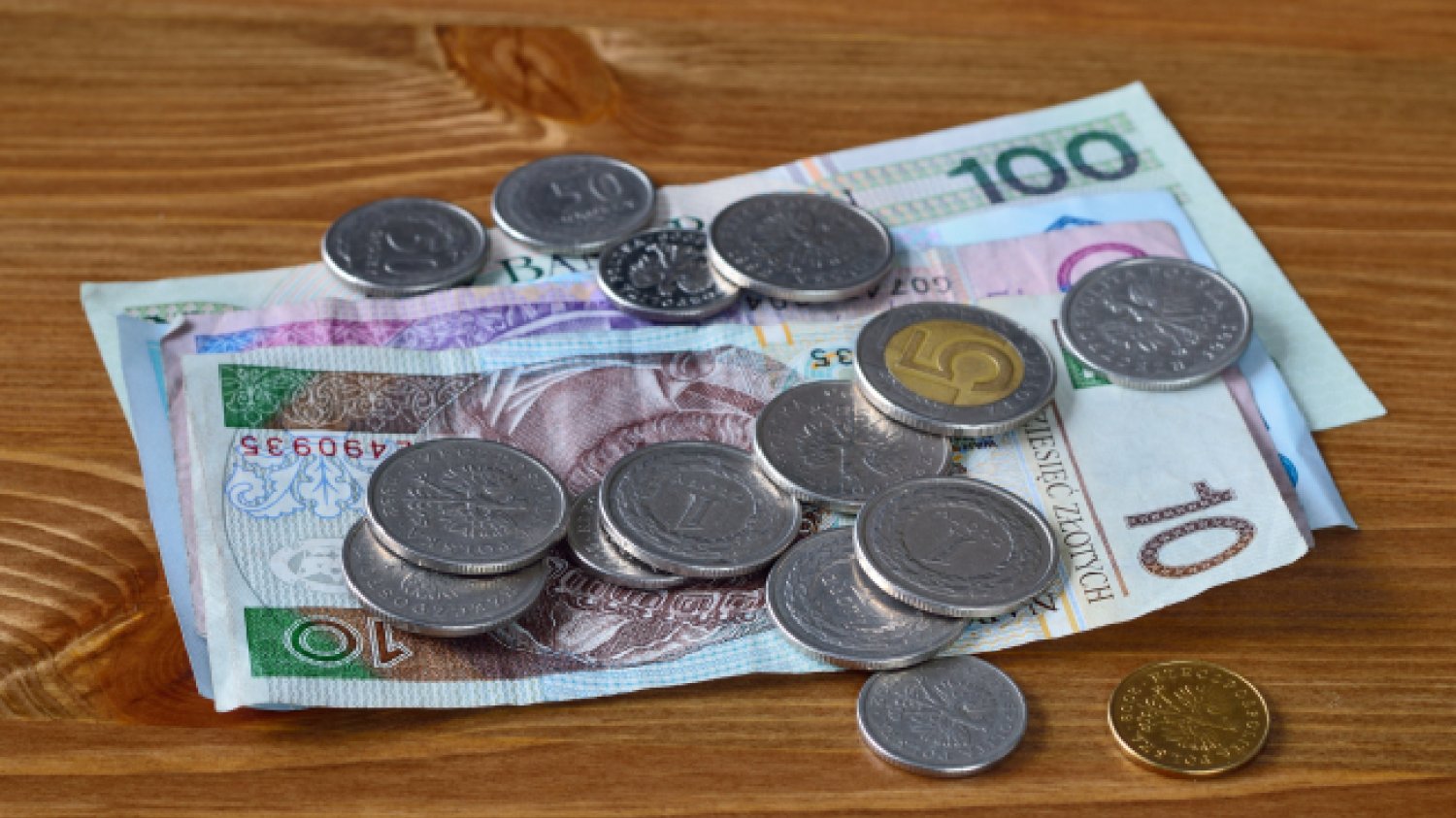 polskie banknoty i złotówki leżą na drewnianym stole
