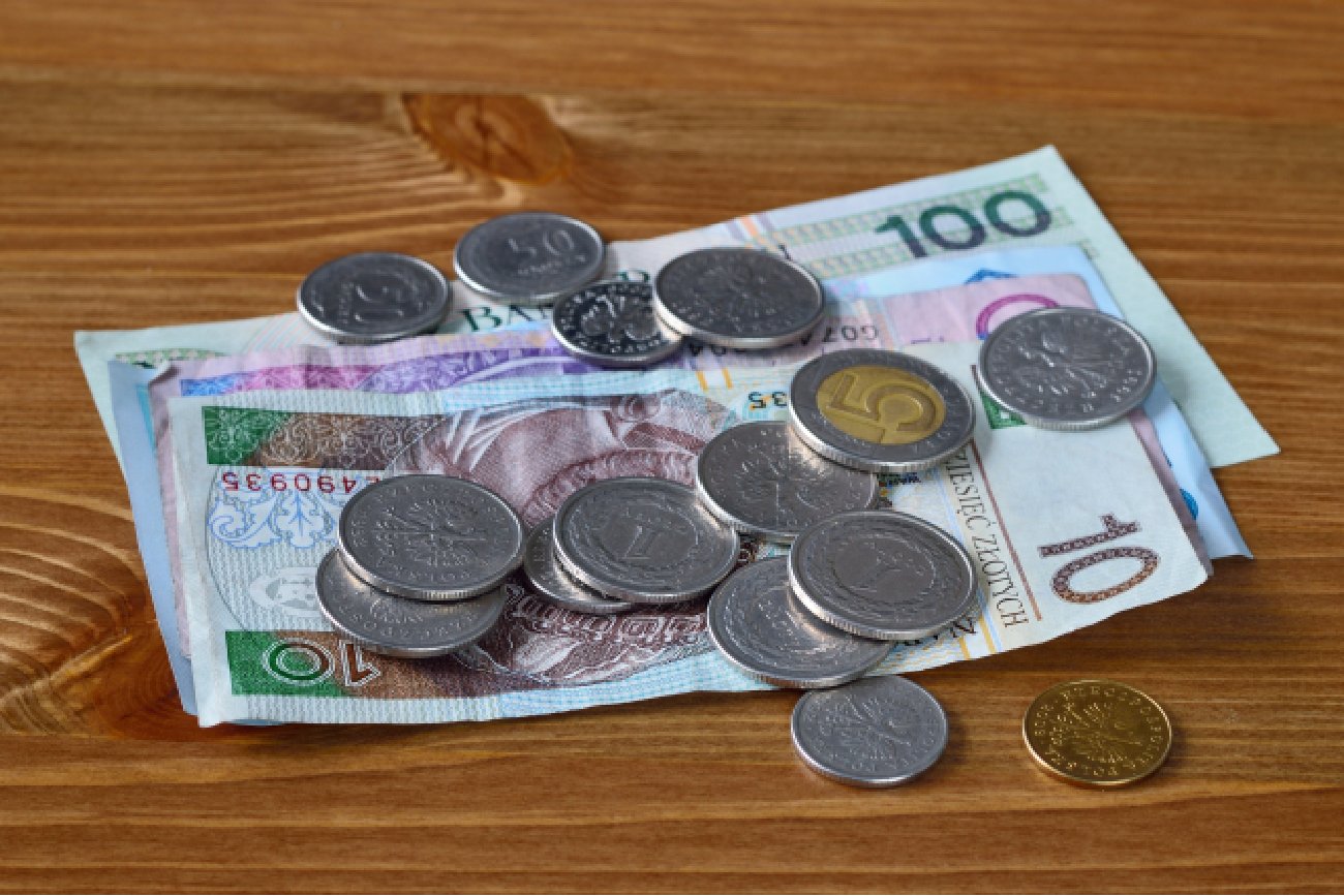 polskie banknoty i złotówki leżą na drewnianym stole