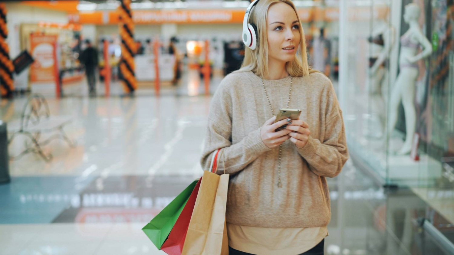 Kobieta ze słuchawkami jest na zakupach. Sieci sklepów w Belgii testują generowanie muzyki z AI.