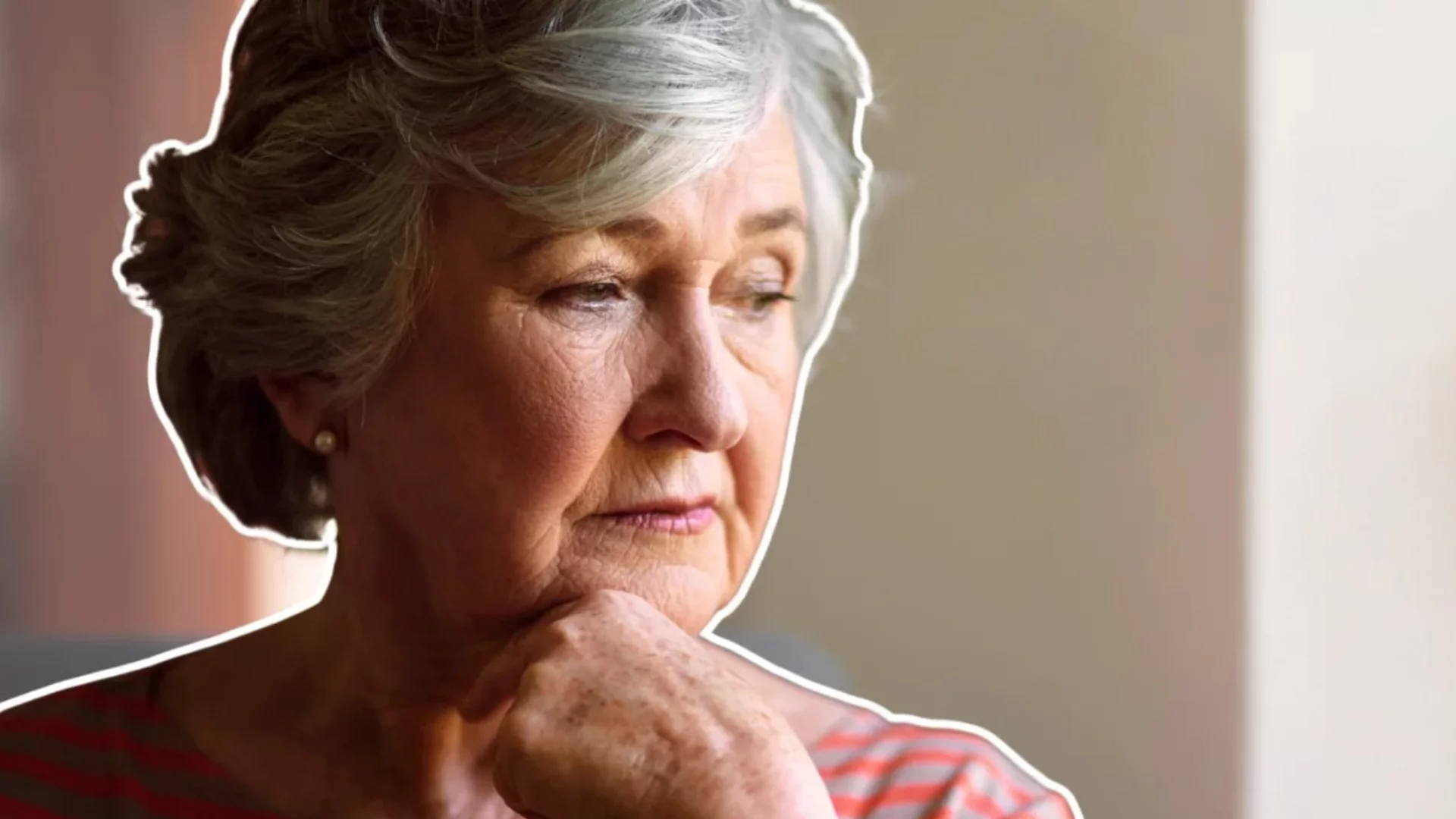 Starsza kobieta patrzy przez okno, smutna.