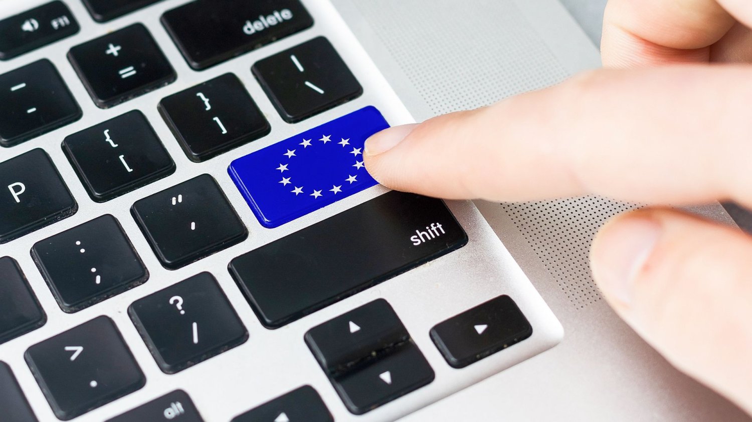 dłoń z palcem wciskającym przycisk z unijną flagą na klawiaturze komputera