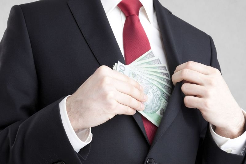 Mężczyzna w garniturze chowa polskie banknoty stuzłotowe do kieszeni marynarki.