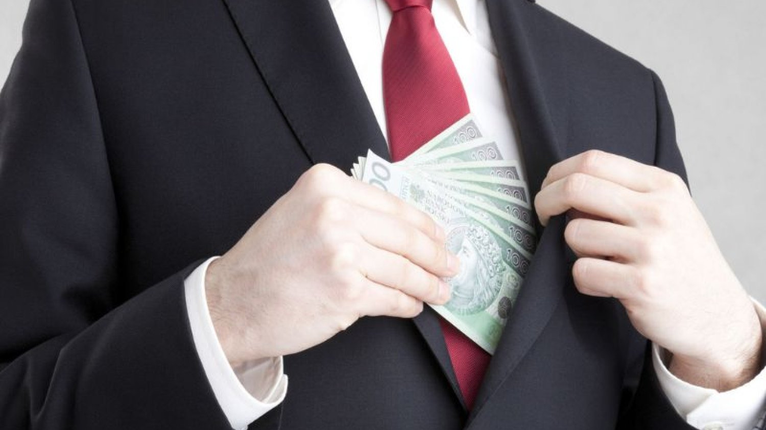 Mężczyzna w garniturze chowa polskie banknoty stuzłotowe do kieszeni marynarki.