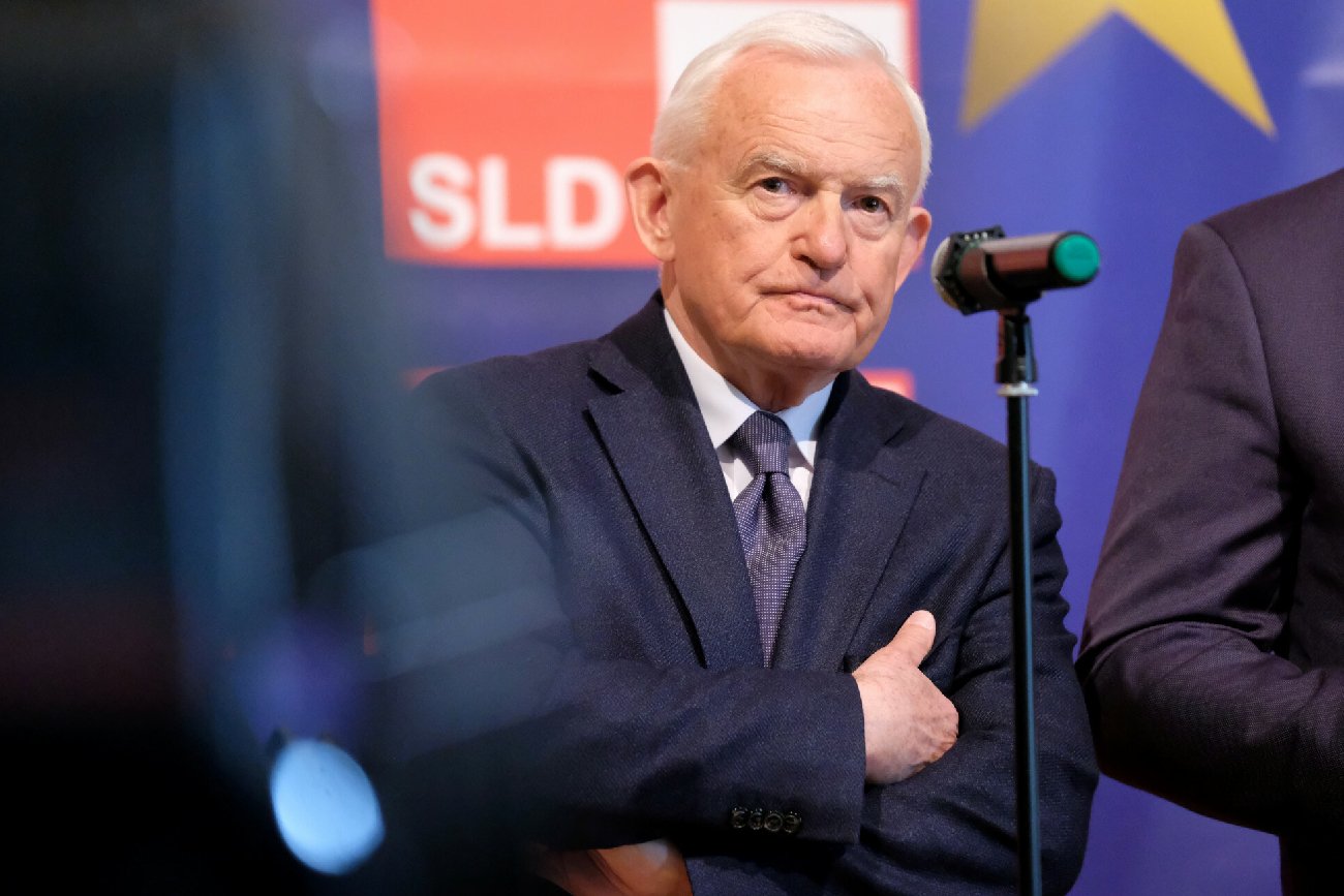 Leczek Miller na konferencji stoi elegancko ubrany przed mikrofonem