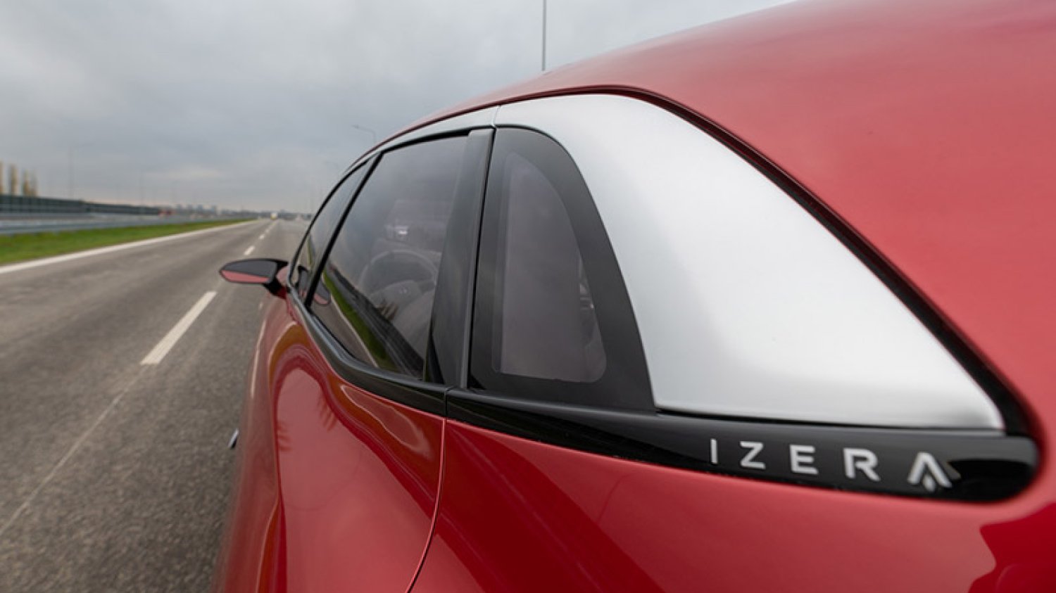 Polski samochód elektryczny Izera na drodze. Czerwony samochód jadący polską autostradą.