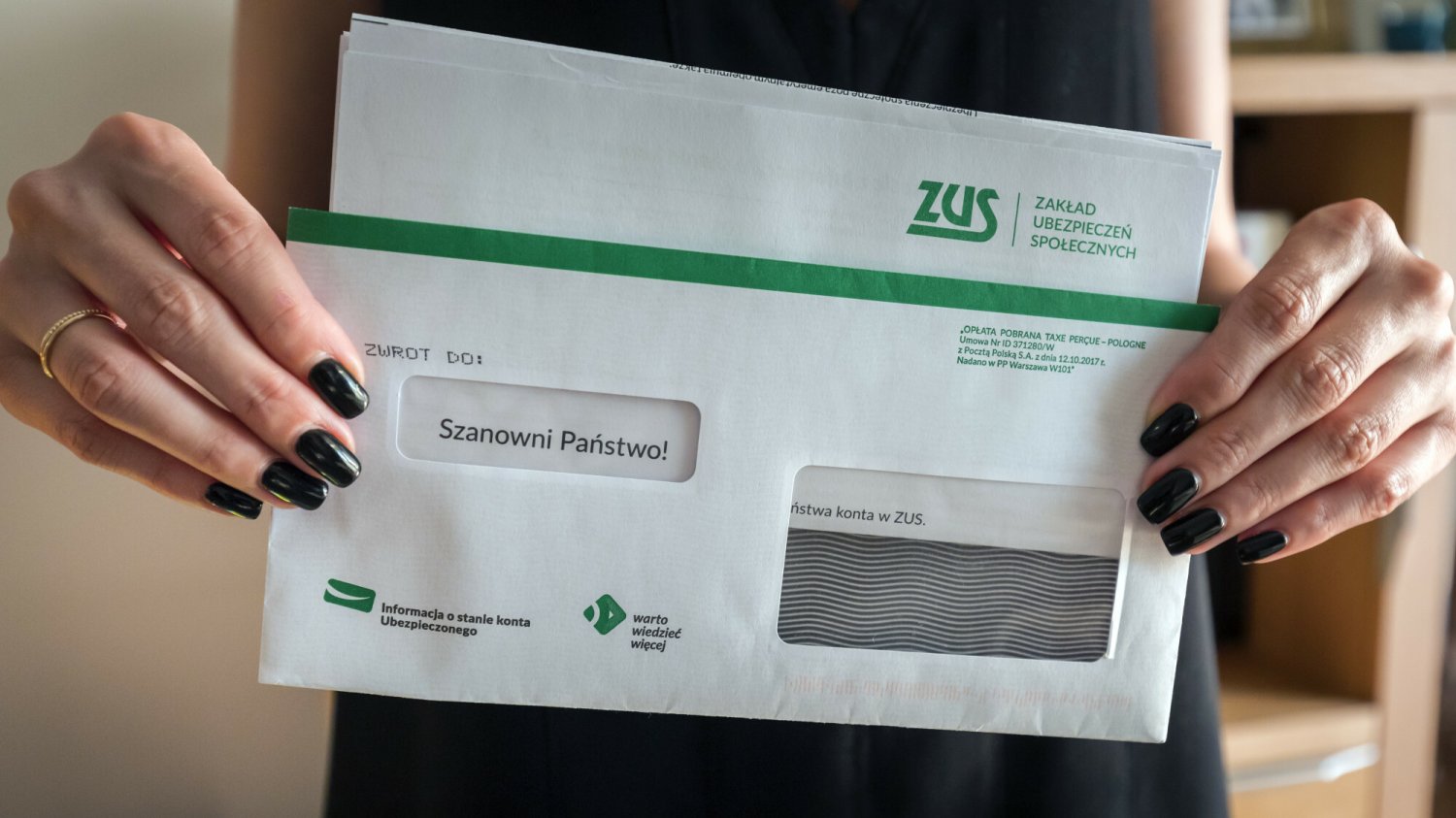 kobieta z czarnym lakierem na paznokciach trzyma w dłoniach białą kopertę z napisem ZUS