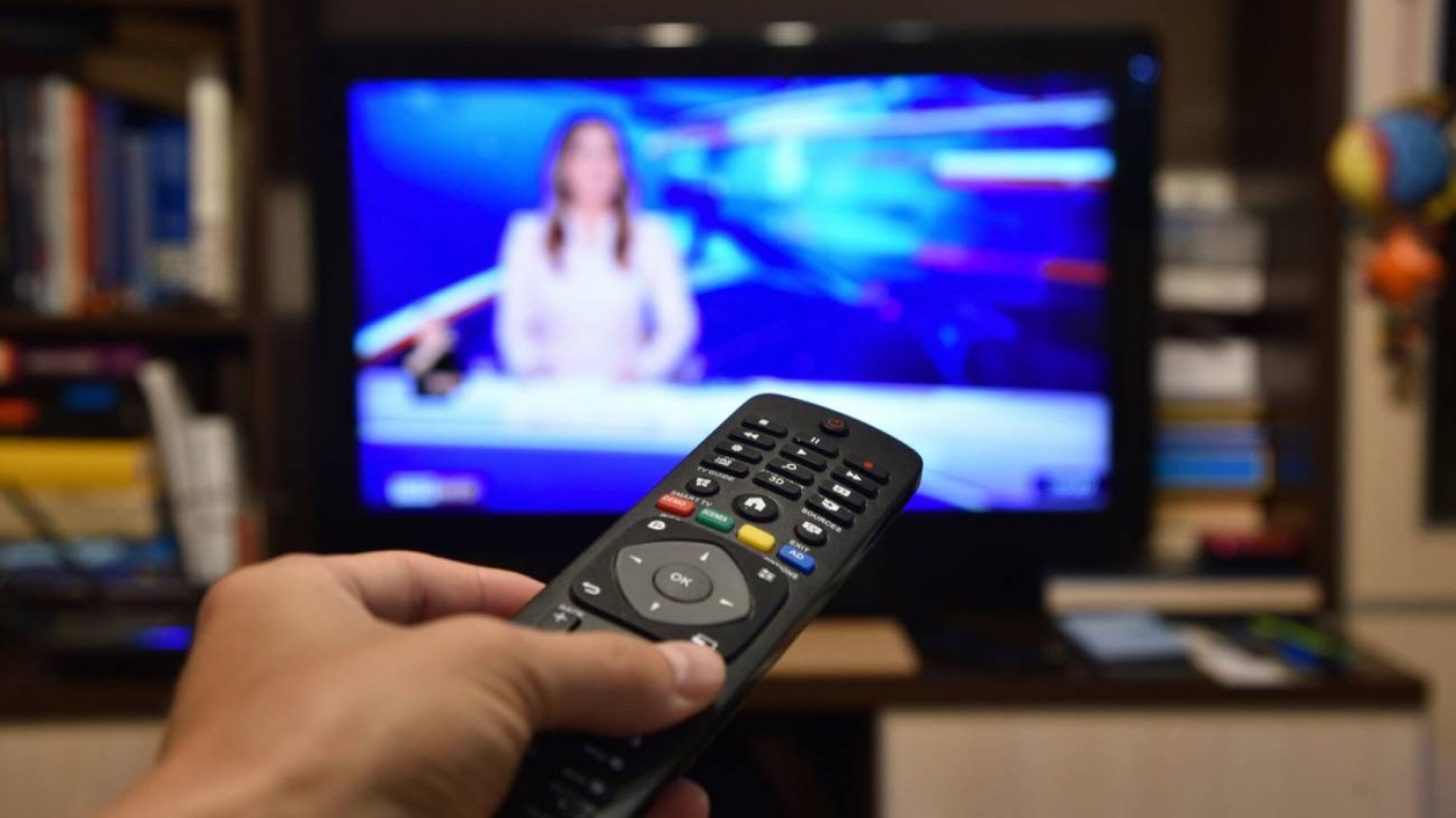 Osoba z pilotem ogląda TVP Info.