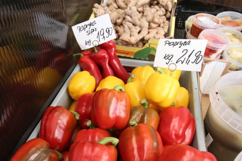 Warzywa wyłożone na stoisku na rynku. Na pierwszym planie papryki z kartkami, na których wypisana jest cena za kilogram.