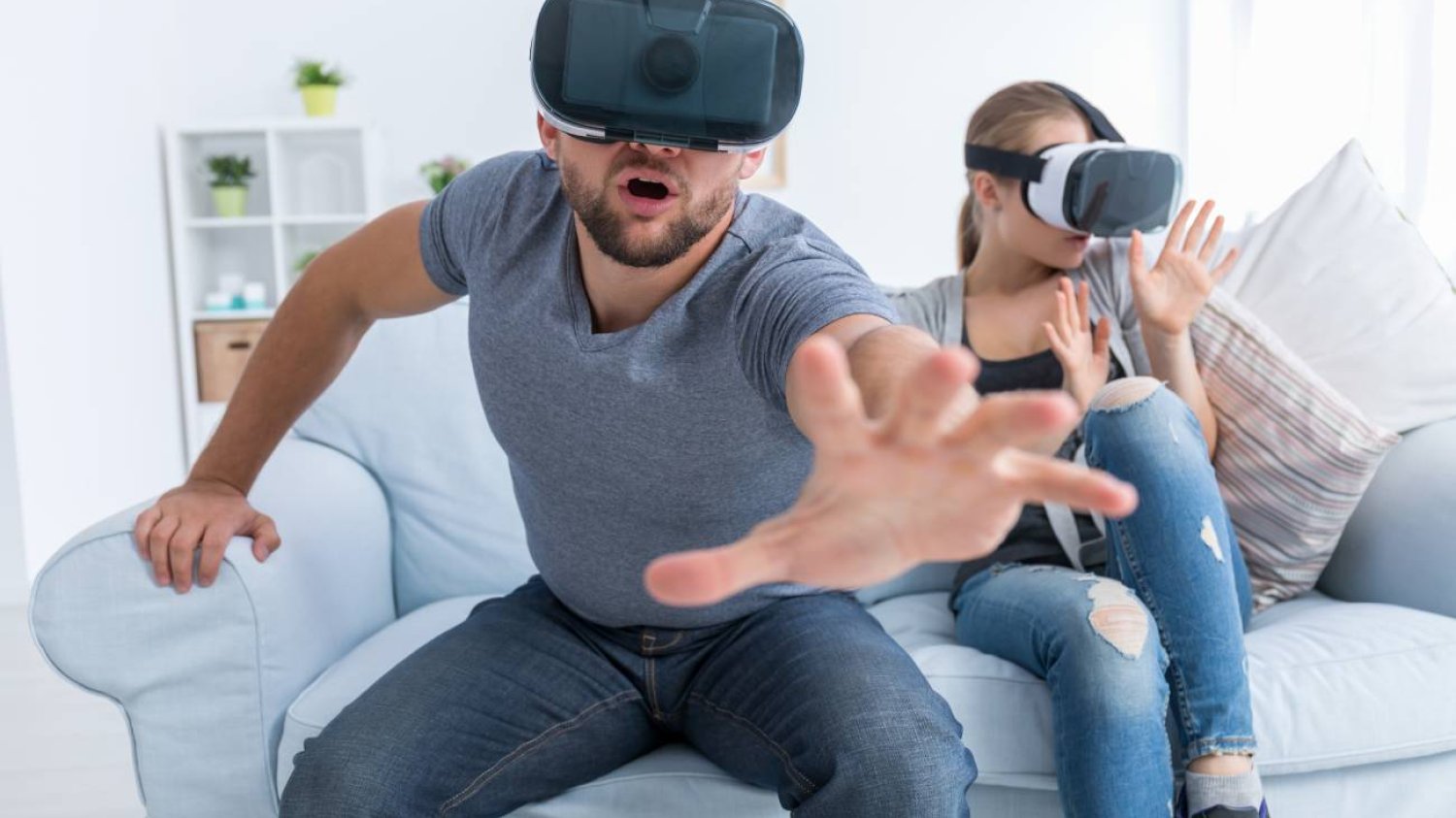 Para w goglach VR siedzi na kanapie i się bawi.